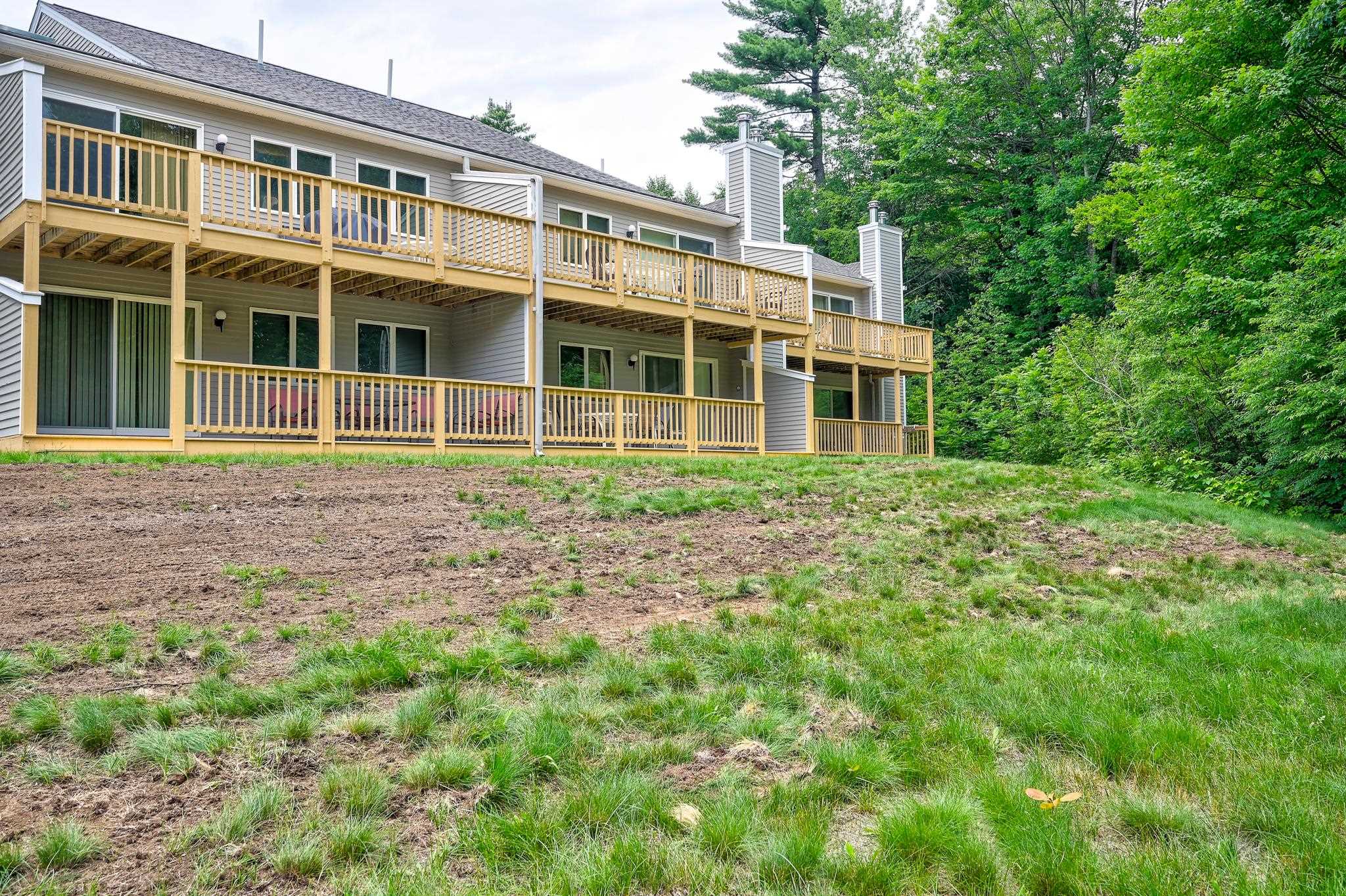 Gray condominium building with tiered wooden decks above a sloping lawn and wooded backdrop.