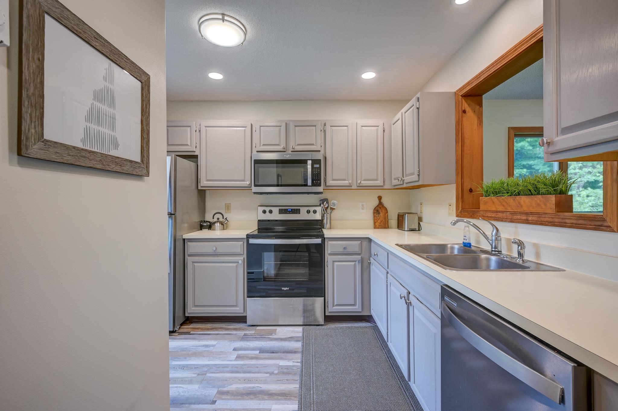 Kitchen with white cabinetry, stainless steel appliances, and a sink beneath a wood-trimmed window.