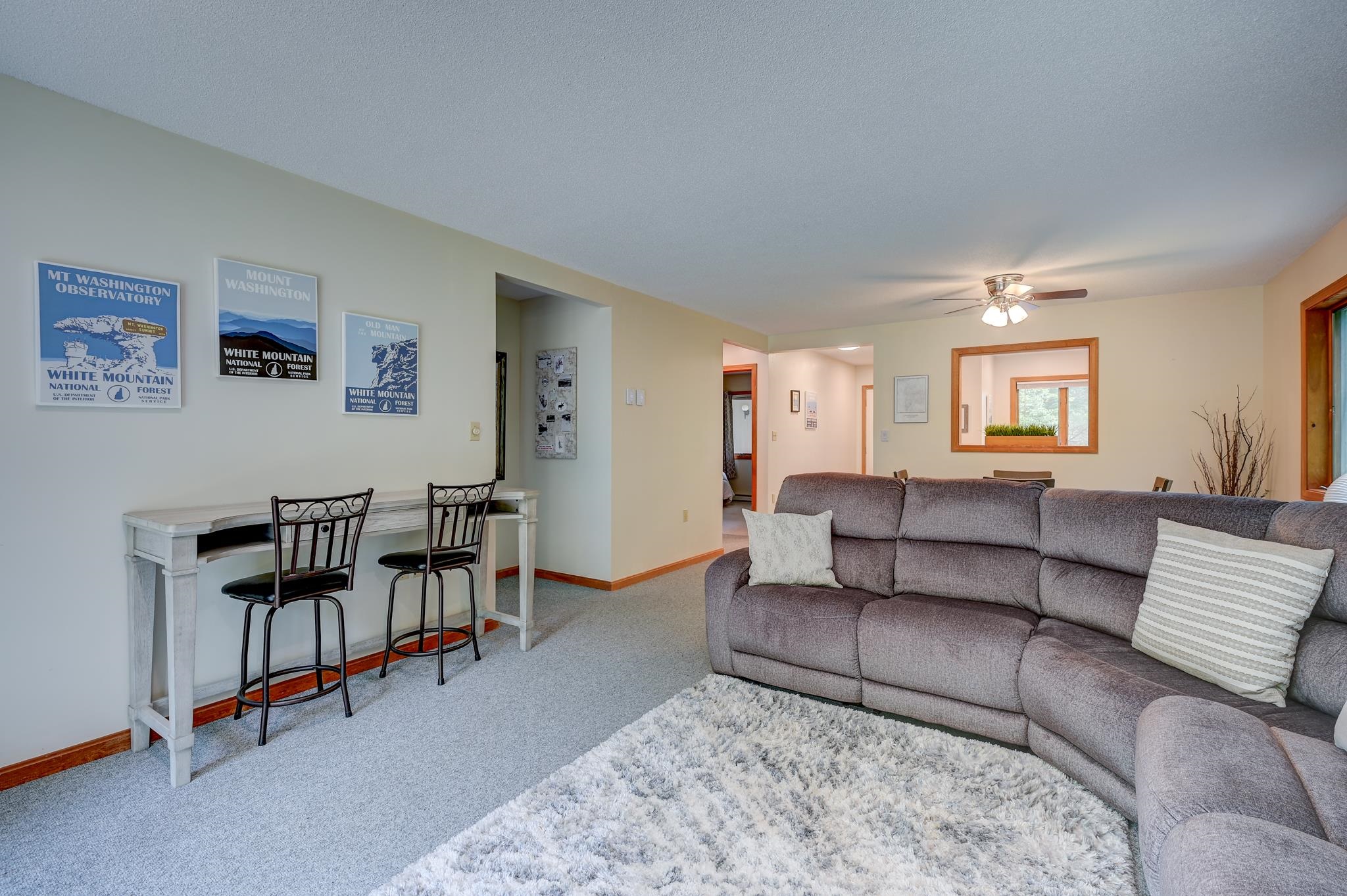 Living room with a gray sectional sofa, white shag rug, and White Mountain posters above a console table.
