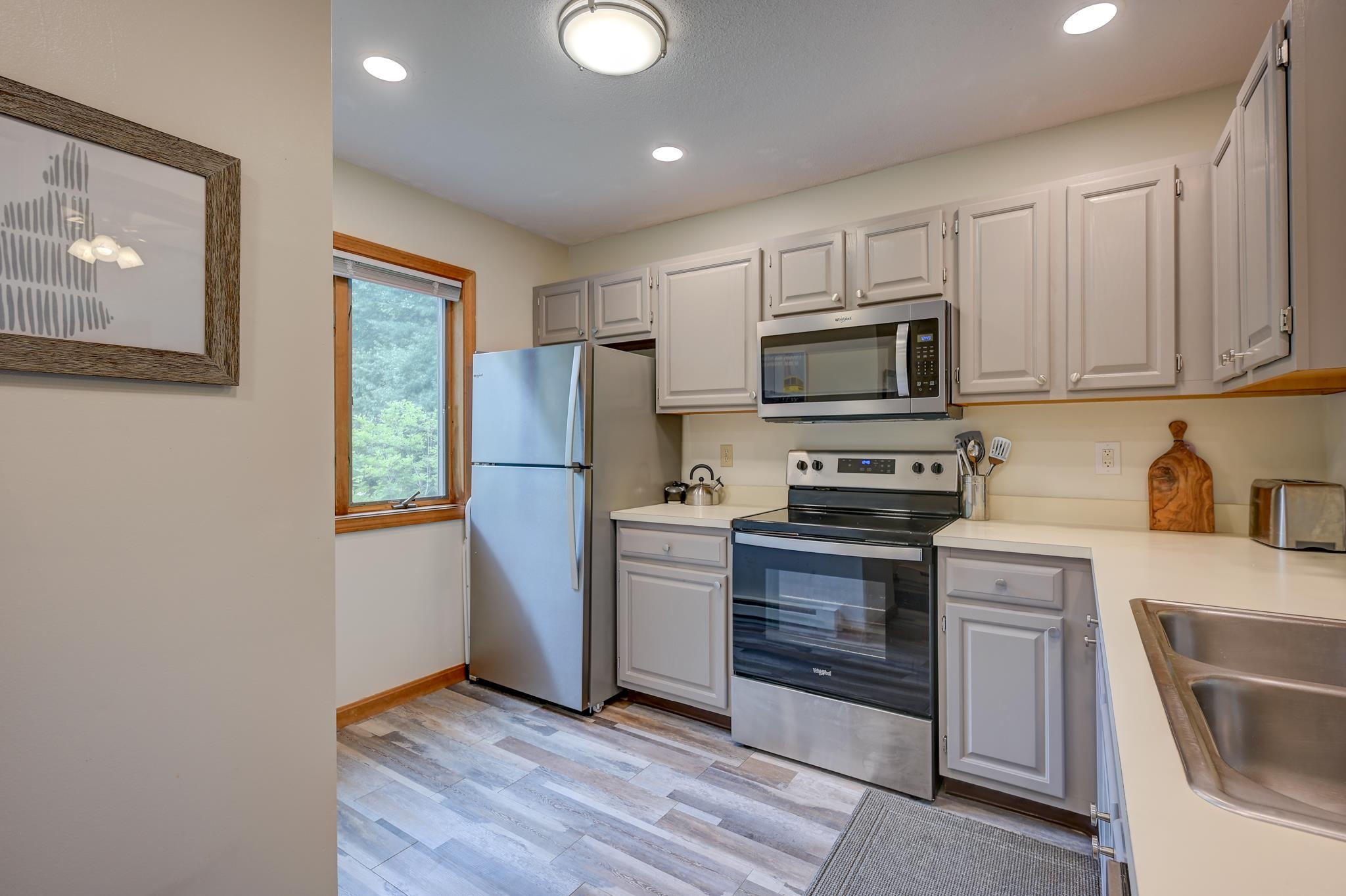 Kitchen with light gray cabinets, stainless steel appliances, and a wood-trimmed window.