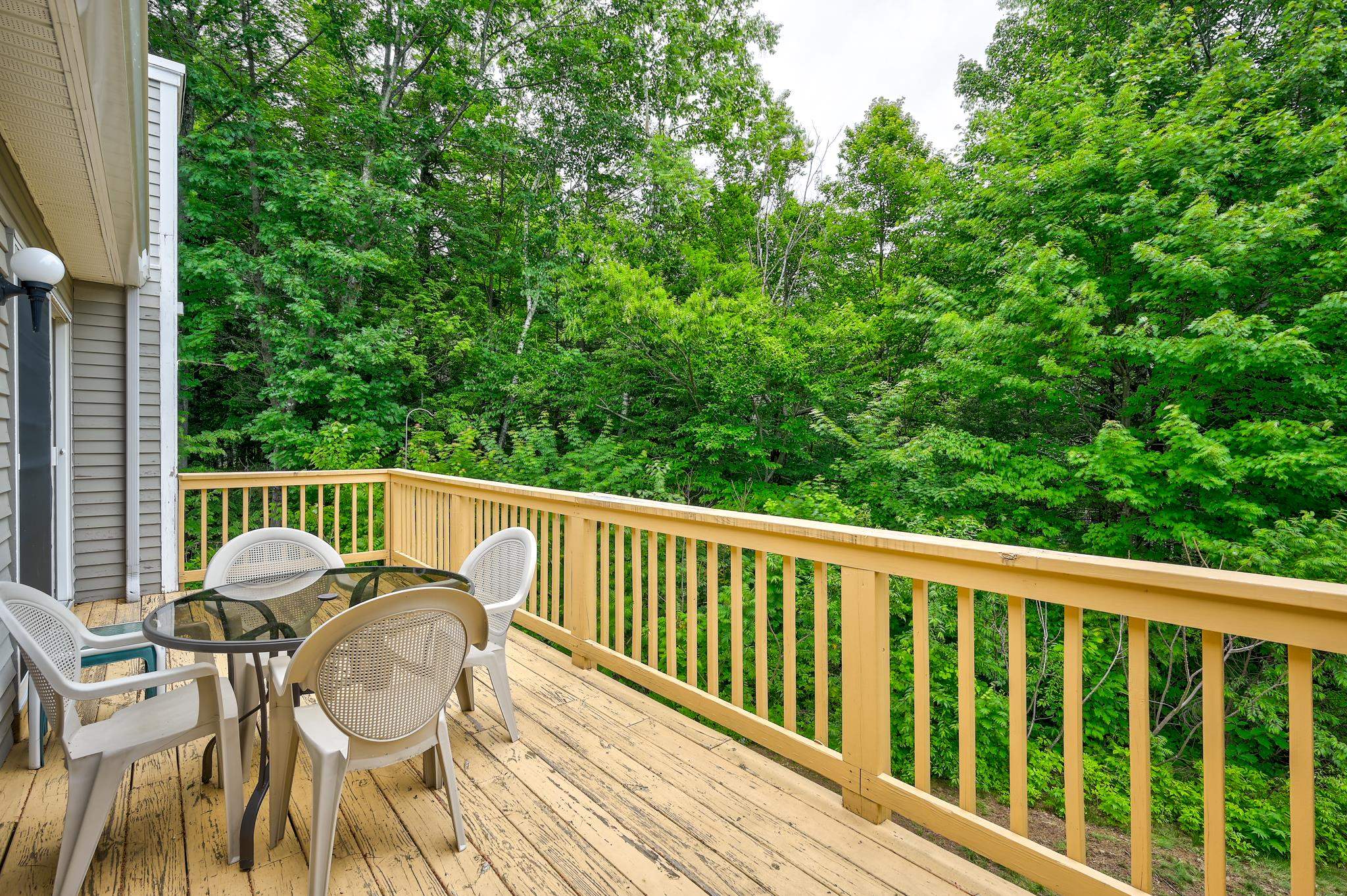 Wood deck furnished with a glass-top table and white chairs, overlooking dense green woods.