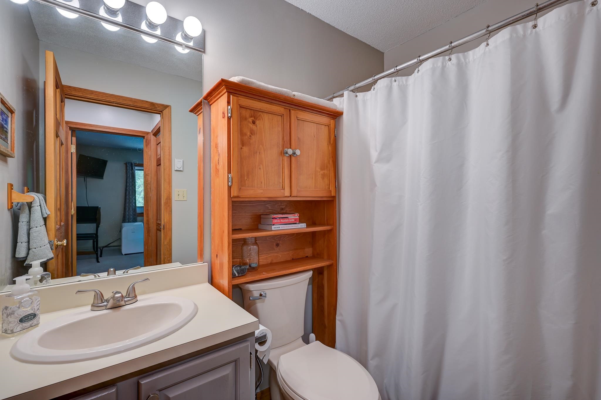 Bathroom with a wooden cabinet above the toilet and a white shower curtain.