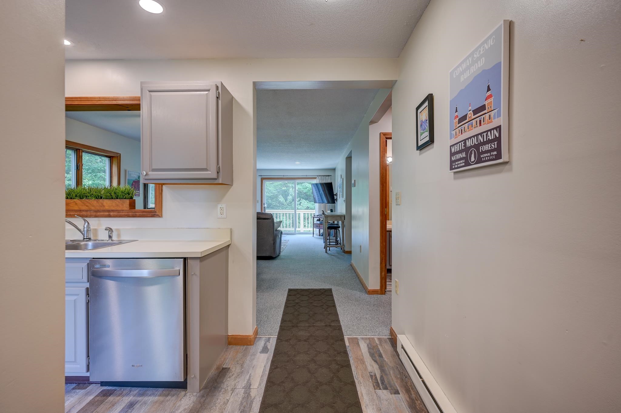 Condo kitchen and hallway opening to a living area with a sliding glass door.