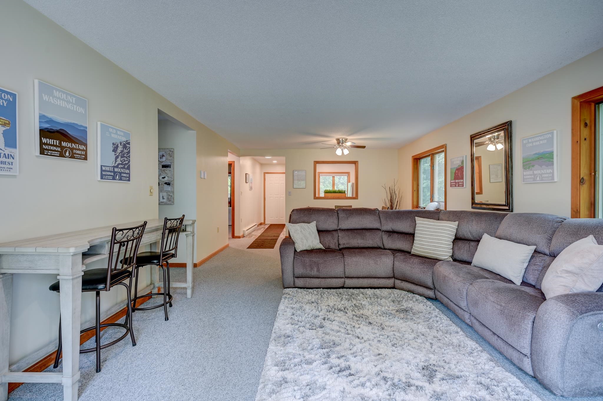 Living room with a large gray sectional, light rug, white desk, and White Mountain posters.