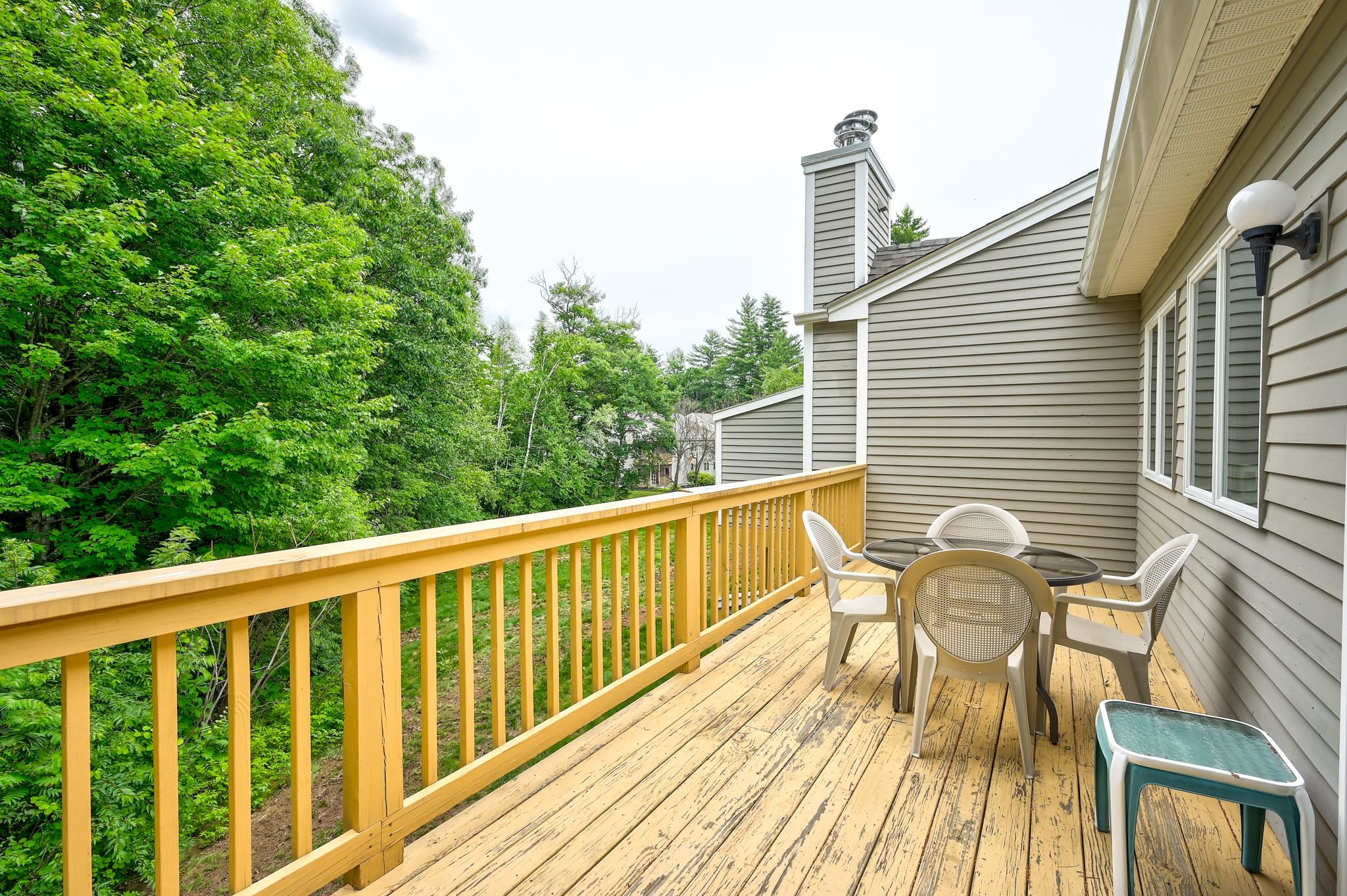 Wooden deck with patio seating beside a gray-sided home, overlooking leafy trees.