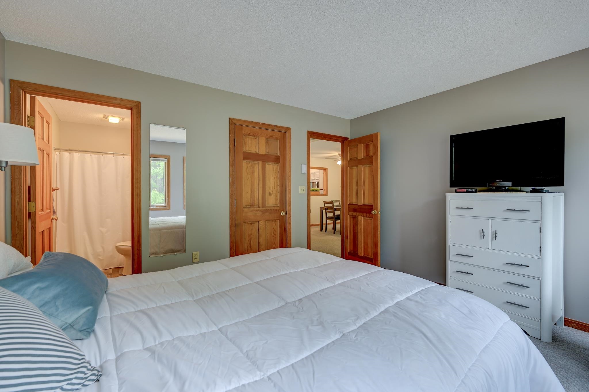 Bedroom with a white quilted bed, wood-trimmed doorways, and a TV on a white dresser.