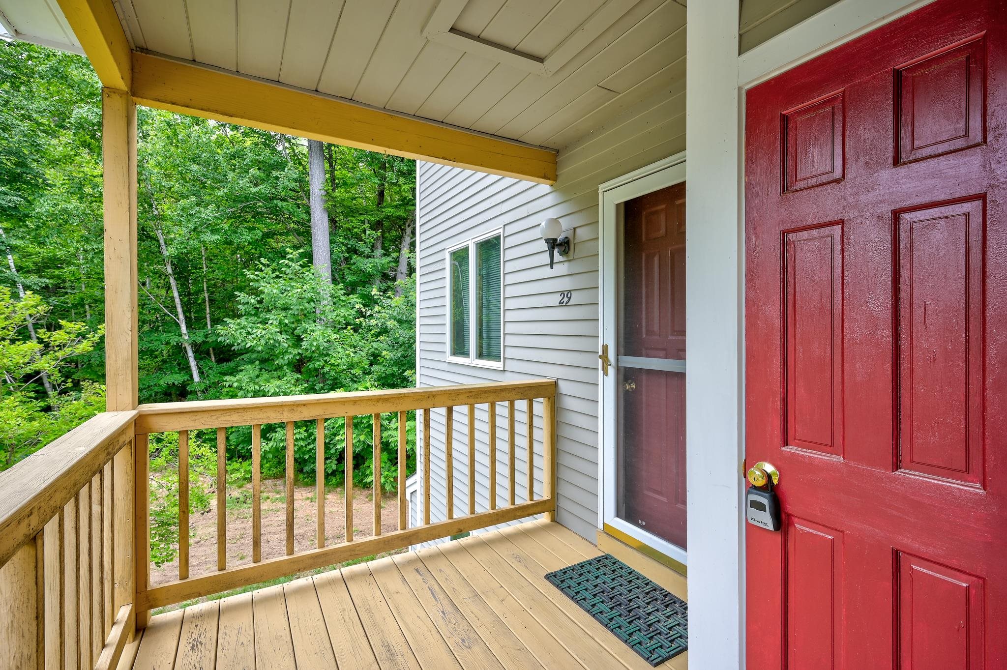 Covered entrance to unit 29 with a red door, wooden porch, and wooded surroundings.