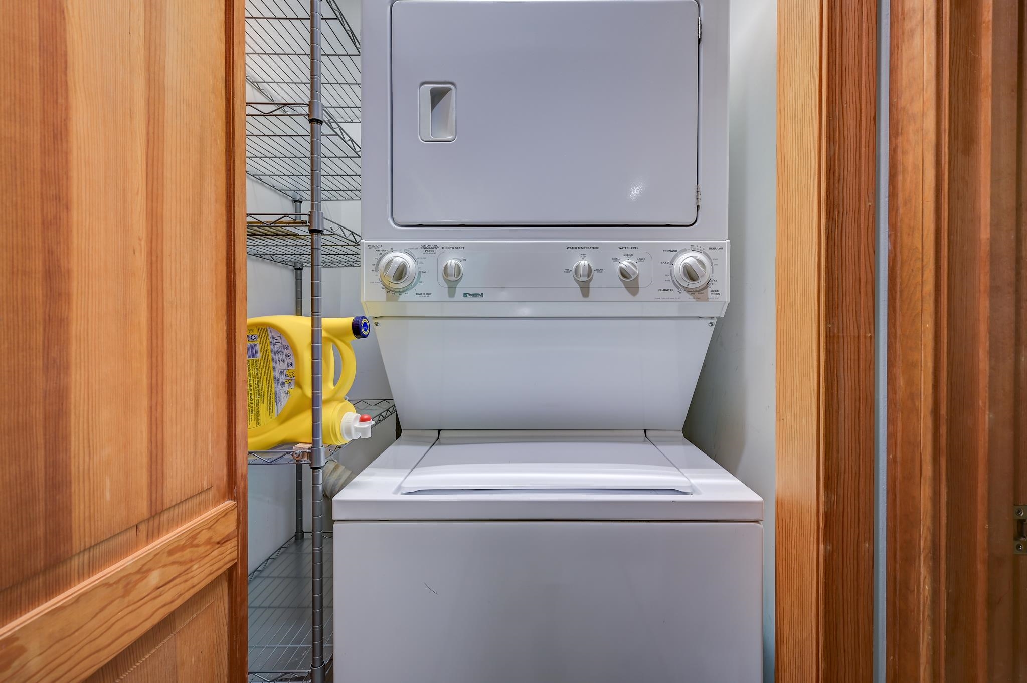 Stacked Kenmore washer and dryer in a laundry closet beside wire shelving and detergent.