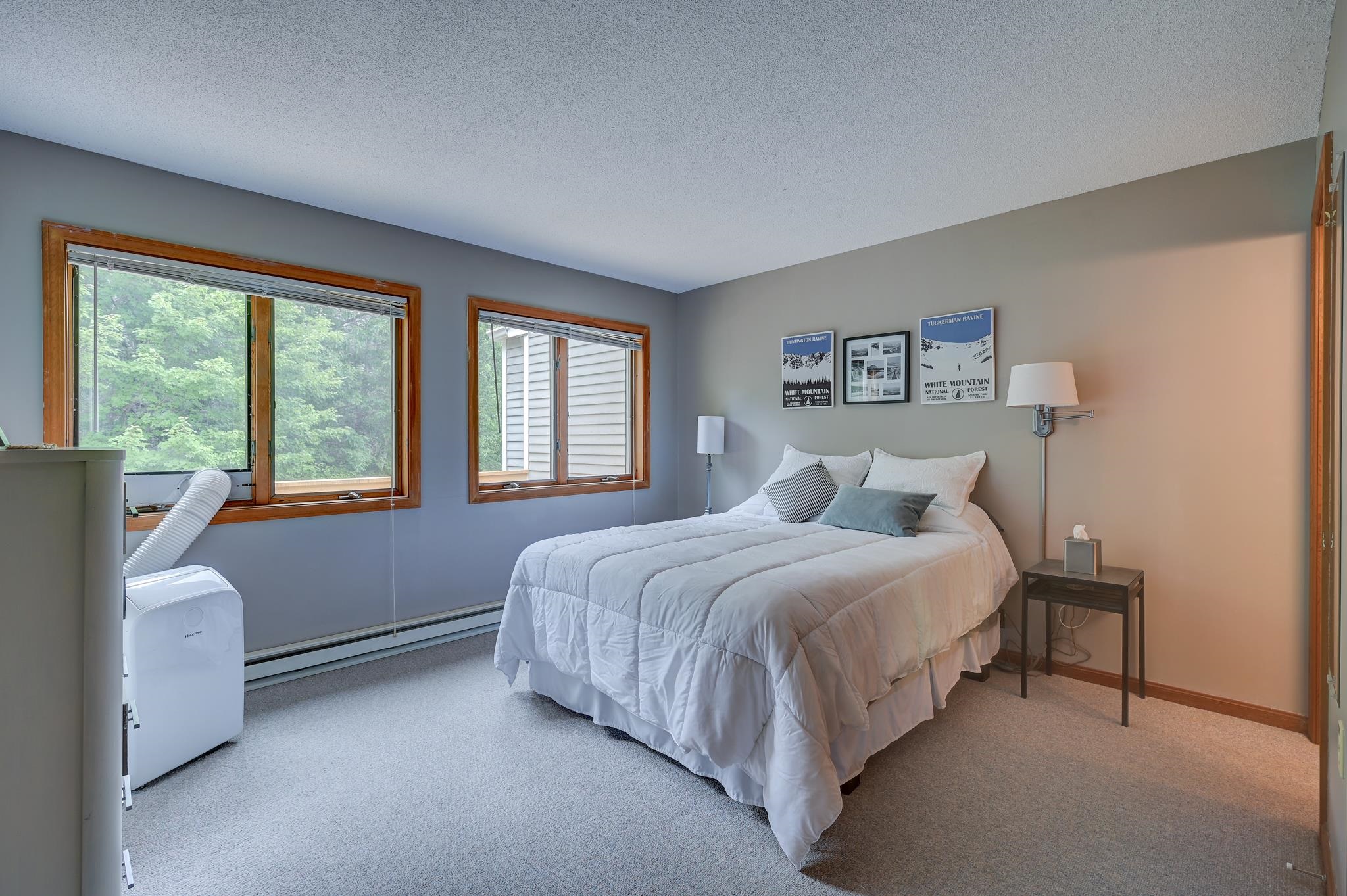 Bedroom with a white bed, wood-trimmed windows, and mountain-themed prints above the headboard.