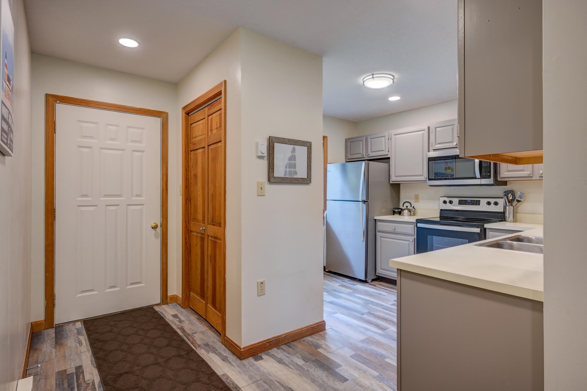 Entry hall opening into a kitchen with plank flooring, white cabinets, stainless steel appliances, and a sink peninsula.