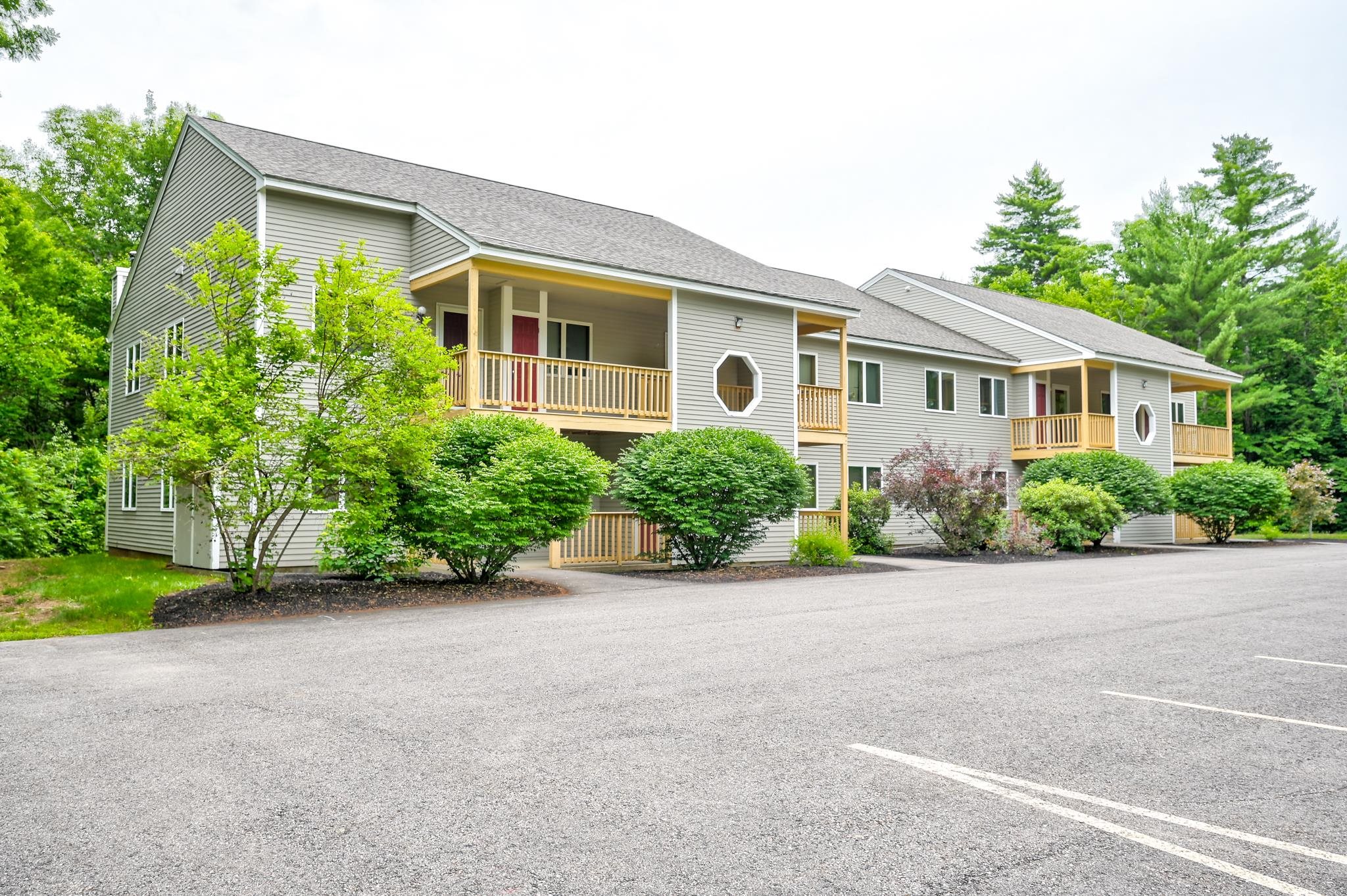 Two-story gray residential building with covered balconies, octagonal windows, and landscaped frontage.