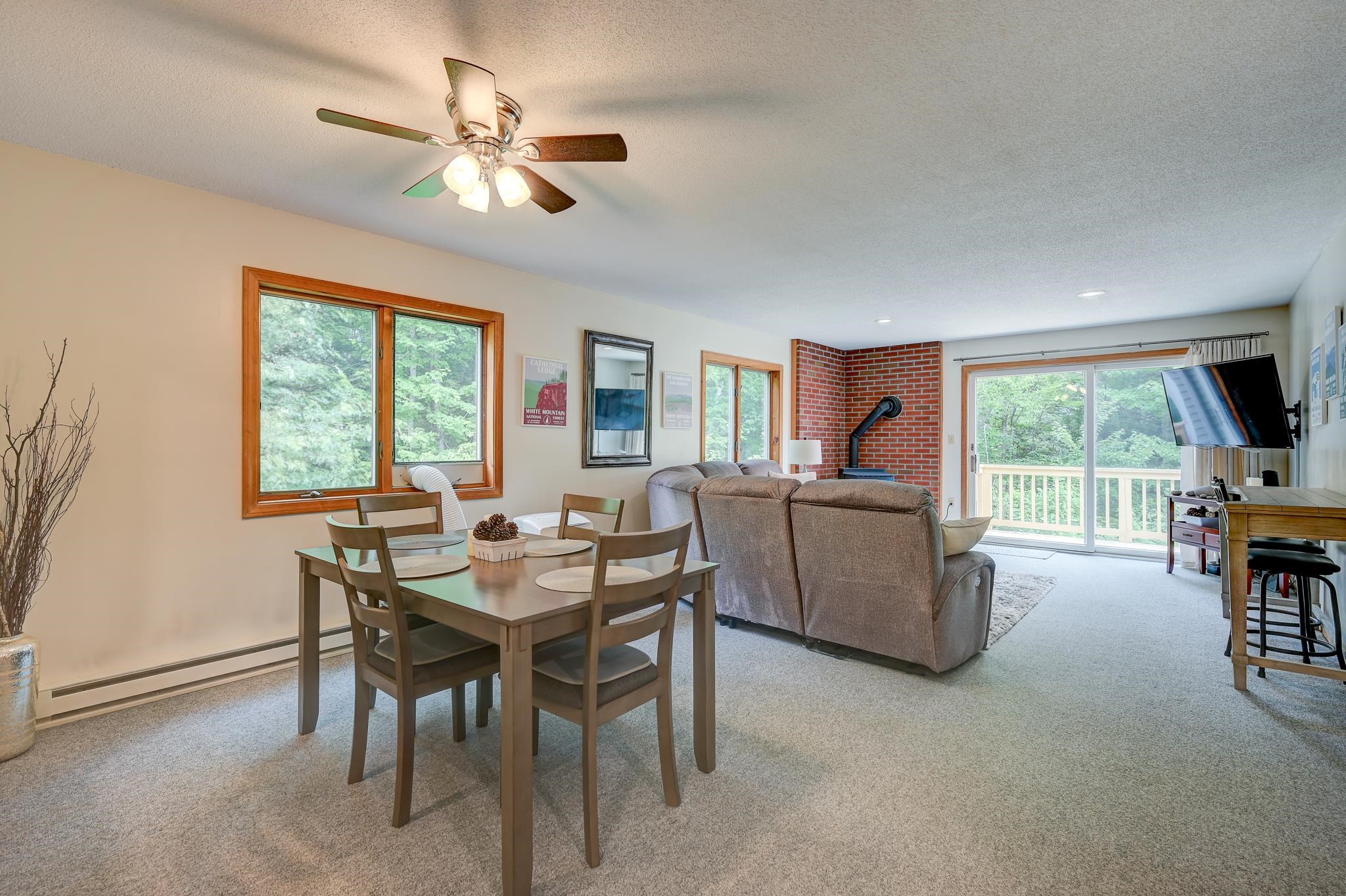 Open-plan living and dining room with a brick fireplace and sliding doors to a wooded view.