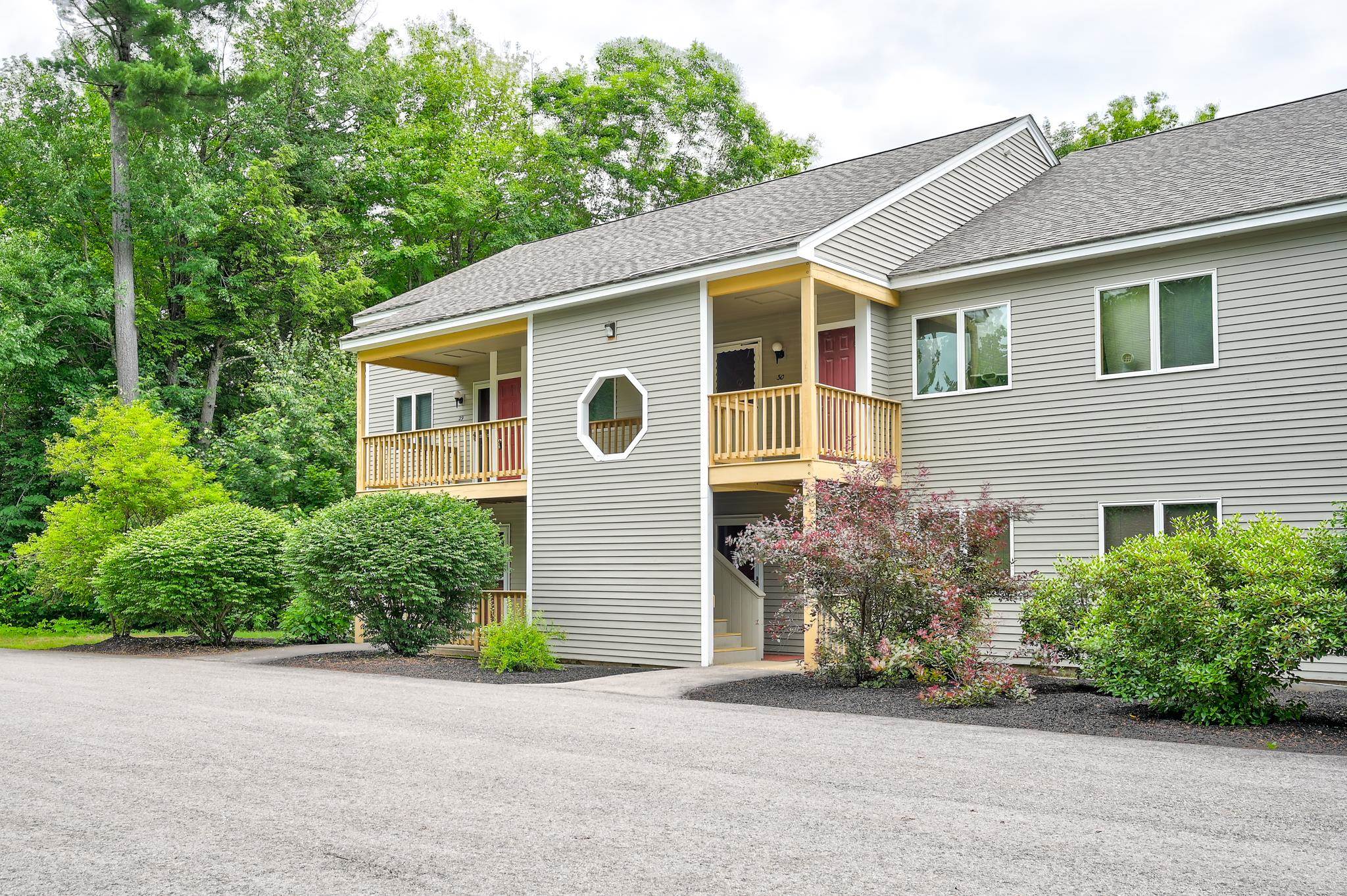 Gray condominium exterior with covered wooden balconies, an octagonal window, and landscaped shrubs.