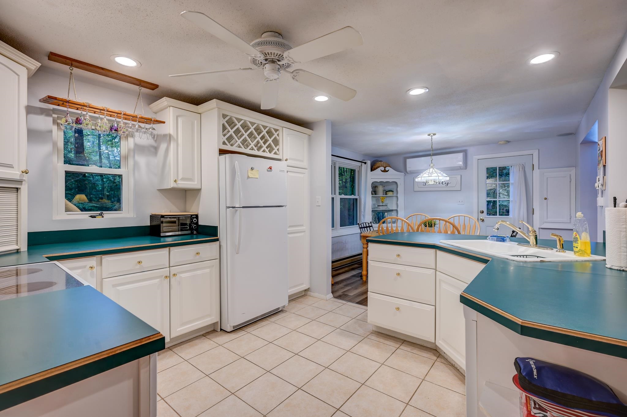 Kitchen with white cabinets and teal countertops opening into a dining area.