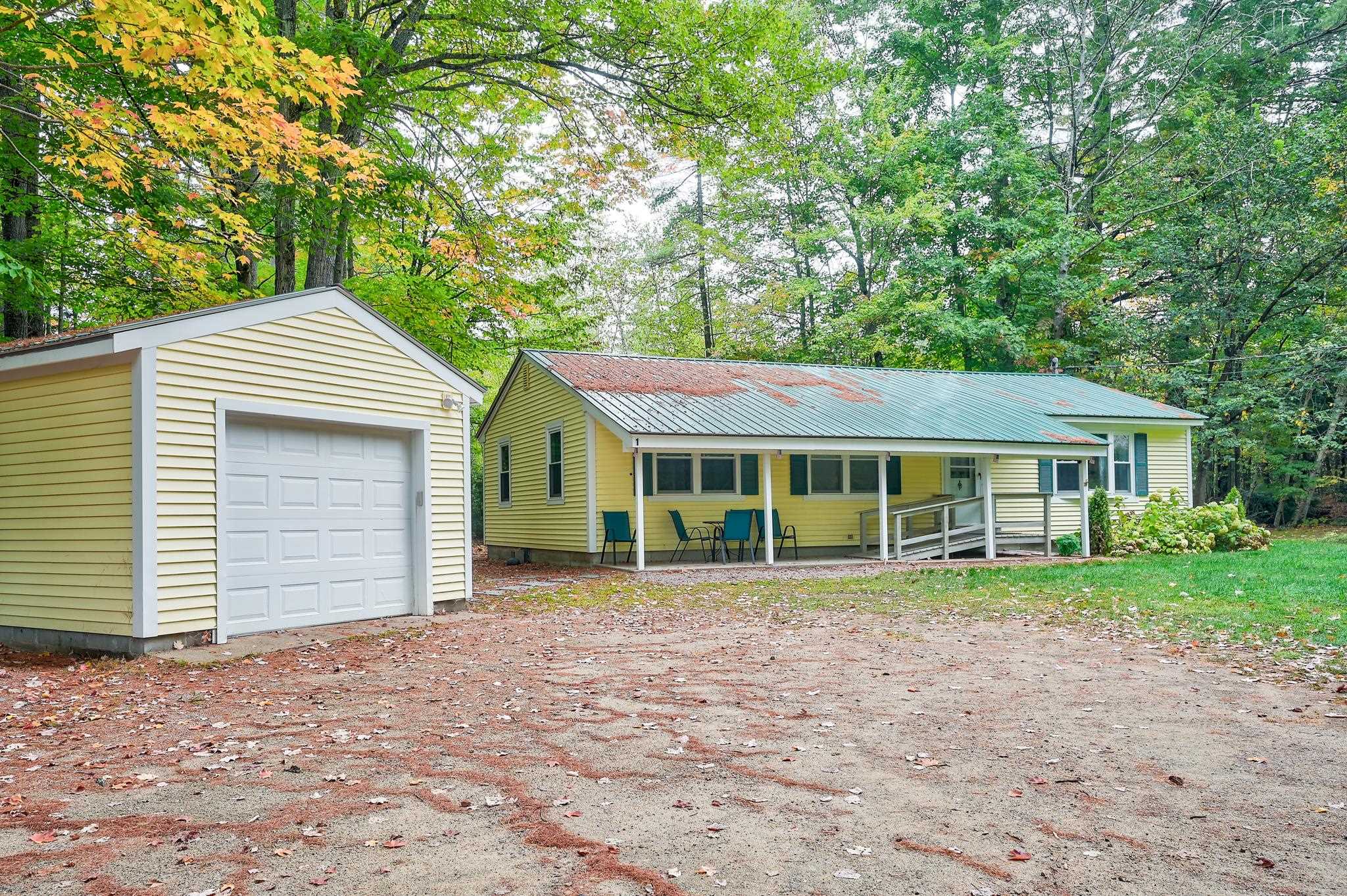 Yellow home with a covered porch and ramp beside a detached garage in a wooded setting.