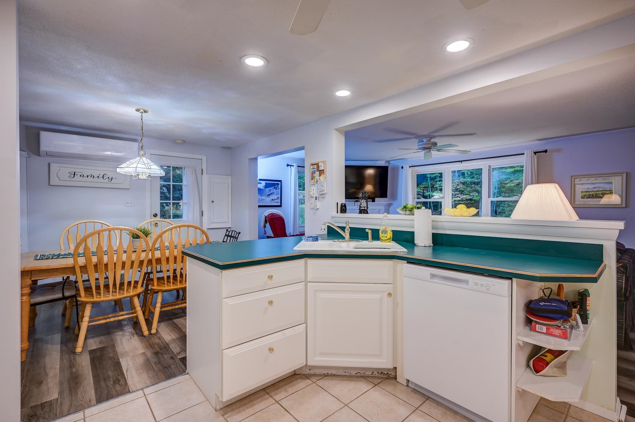 Kitchen with teal countertops and white cabinets, adjoining a dining area with a wooden table and chairs.