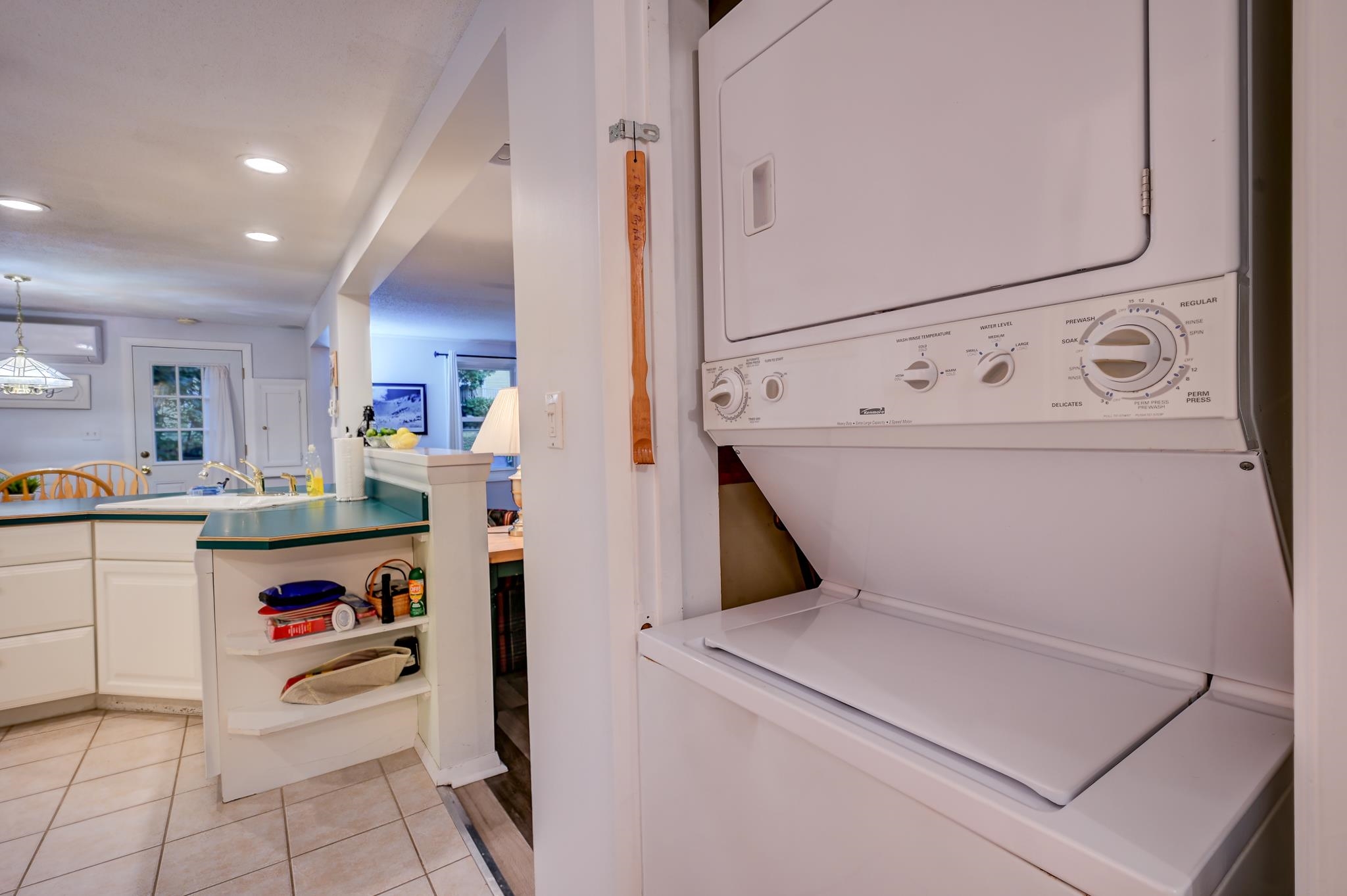 Stacked washer and dryer beside a kitchen with teal countertops and white cabinets.