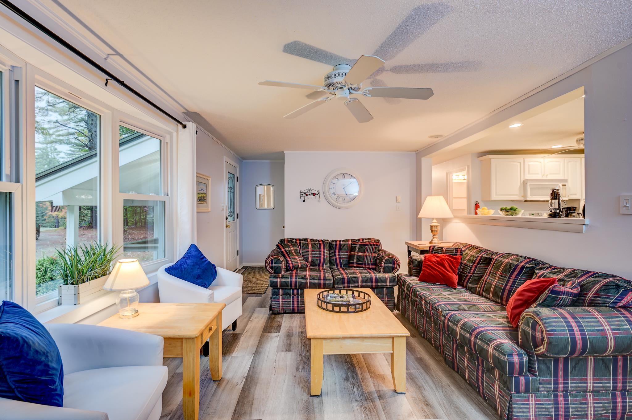 Living room with plaid sofas, white armchairs, large windows, and an open kitchen pass-through.