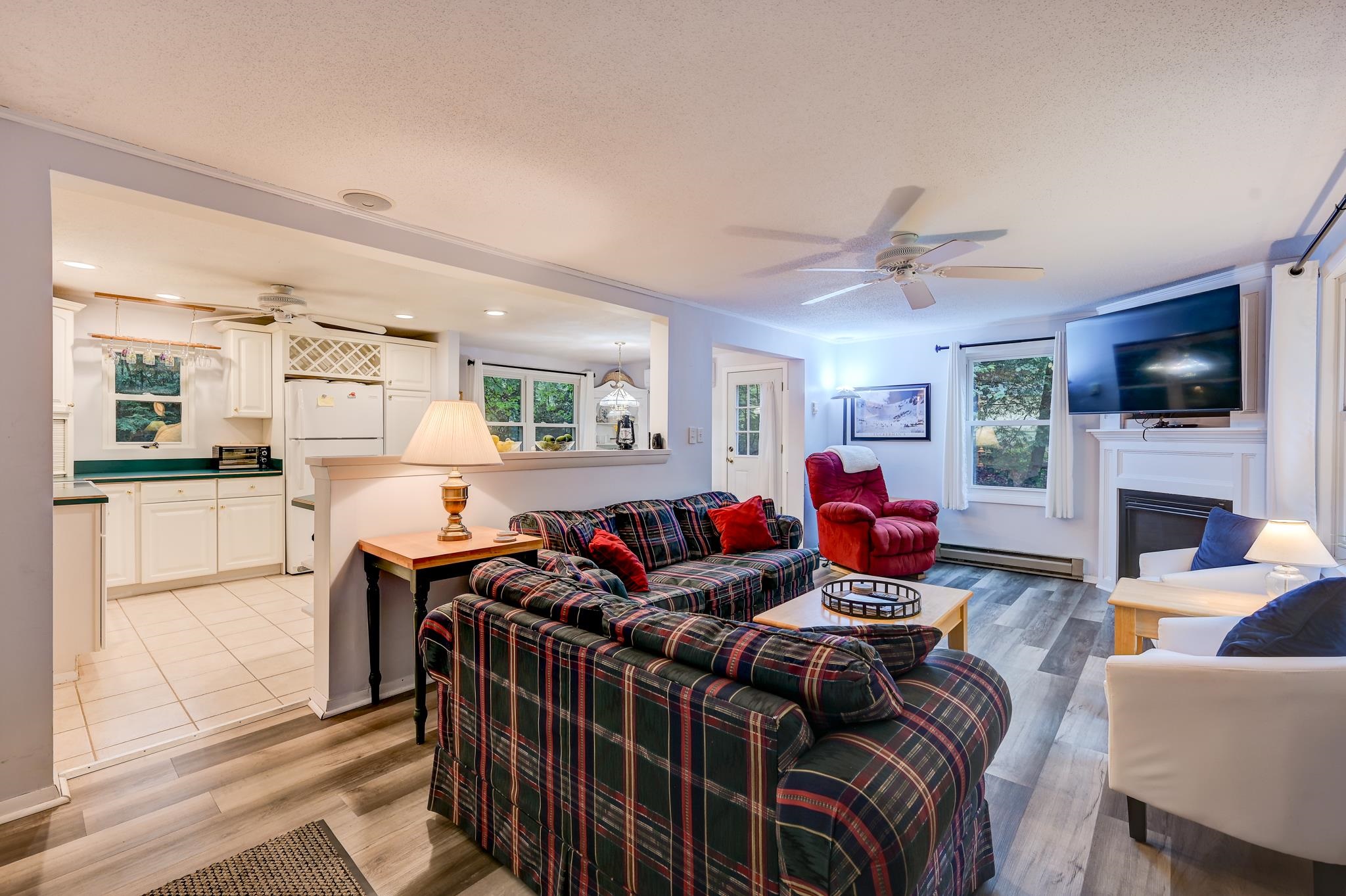 Open-plan living room and kitchen with a plaid sectional, red recliner, and fireplace.