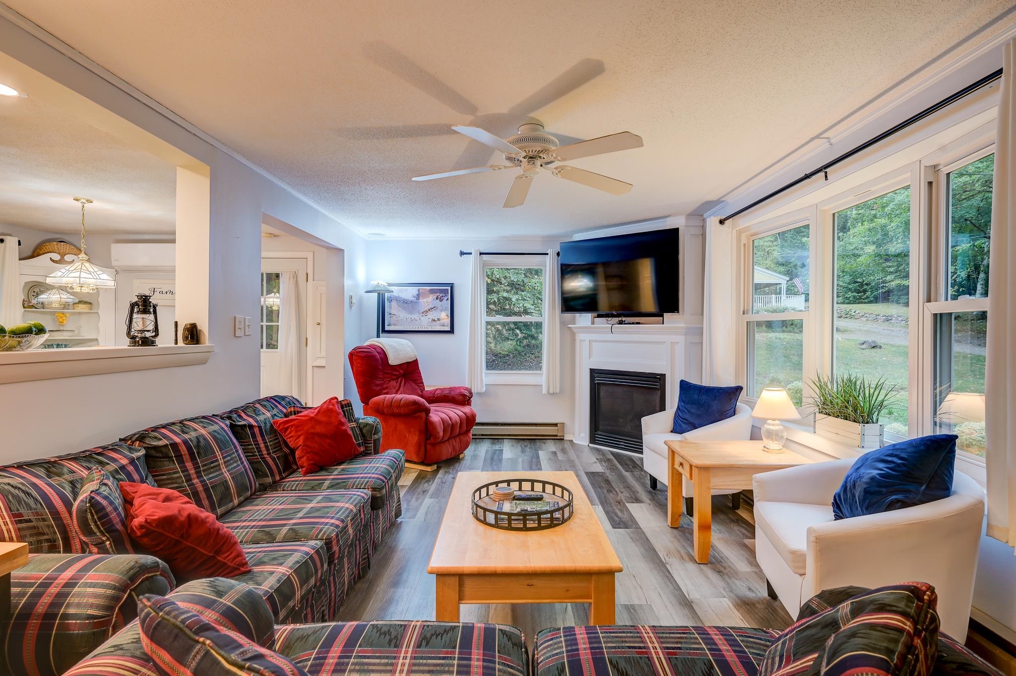 Living room with plaid sofas, red recliner, fireplace, and large windows overlooking a green yard.