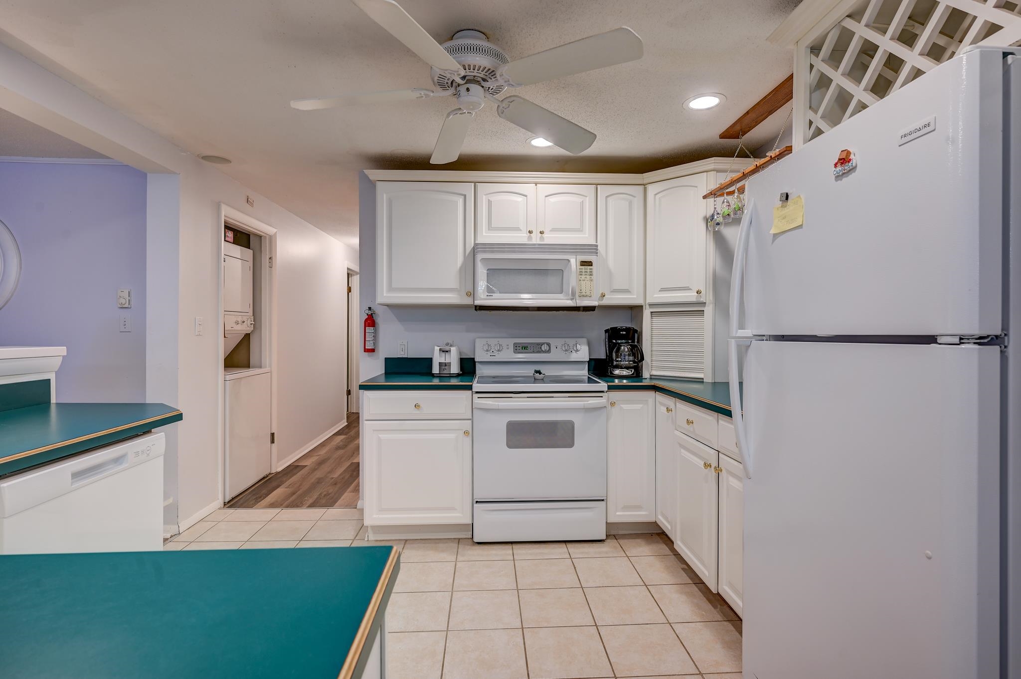 Kitchen with white cabinets, teal countertops, and a large white refrigerator beside the range.