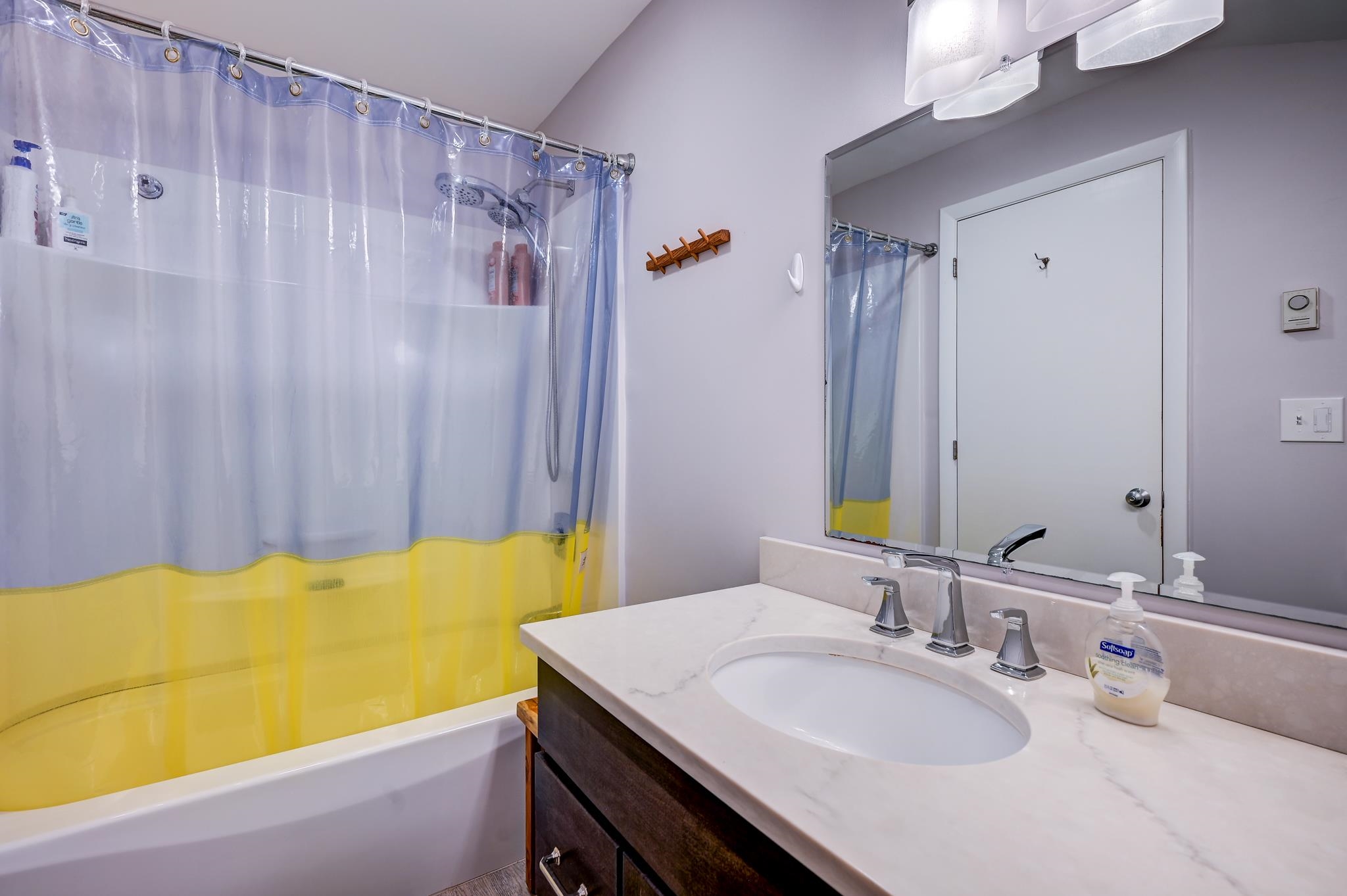 Bathroom with a blue-and-yellow shower curtain, white tub, and dark wood vanity with an oval sink.
