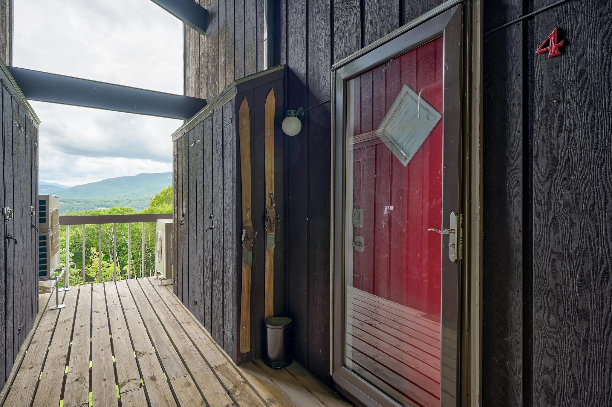 Mountain-view entry deck with a red glass door and vintage skis mounted beside it.