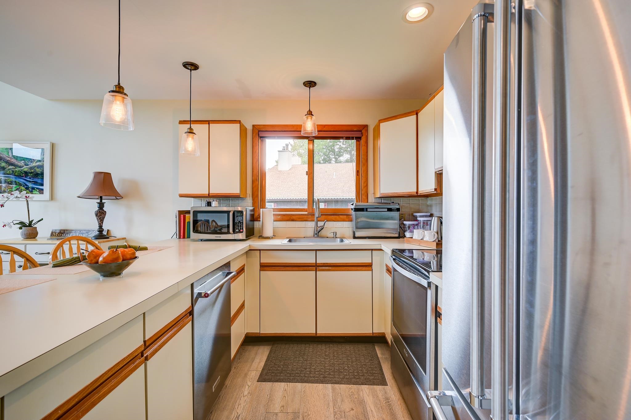 Kitchen with cream cabinets, wood trim, stainless steel appliances, and a window above the sink.