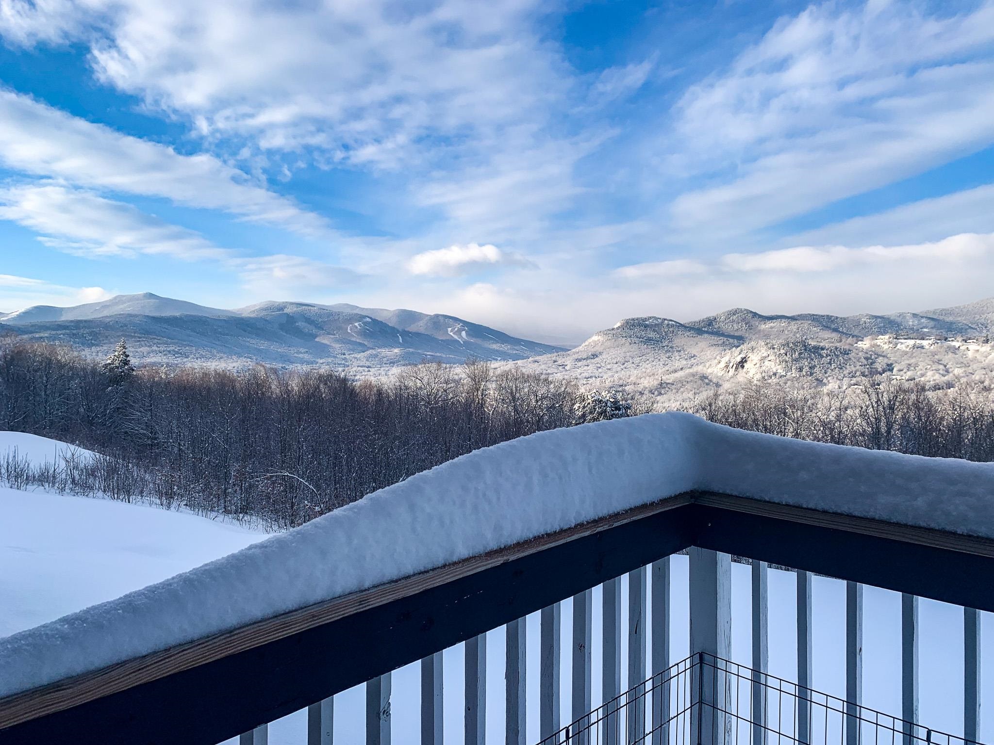 Snow-covered deck railing overlooks a broad winter mountain view.