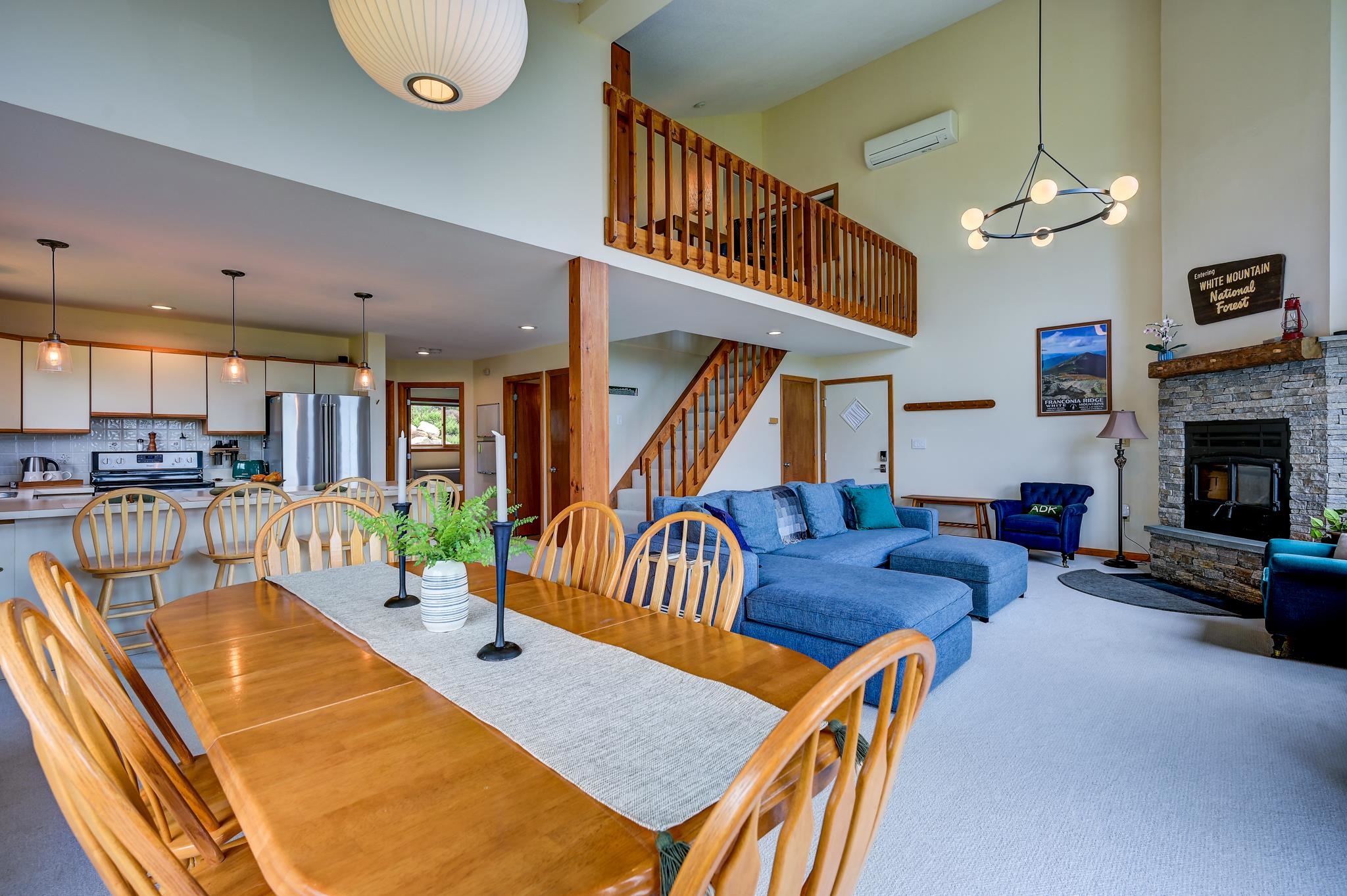 Open-plan living and dining area with a blue sectional, stone fireplace, and wood-railed loft.