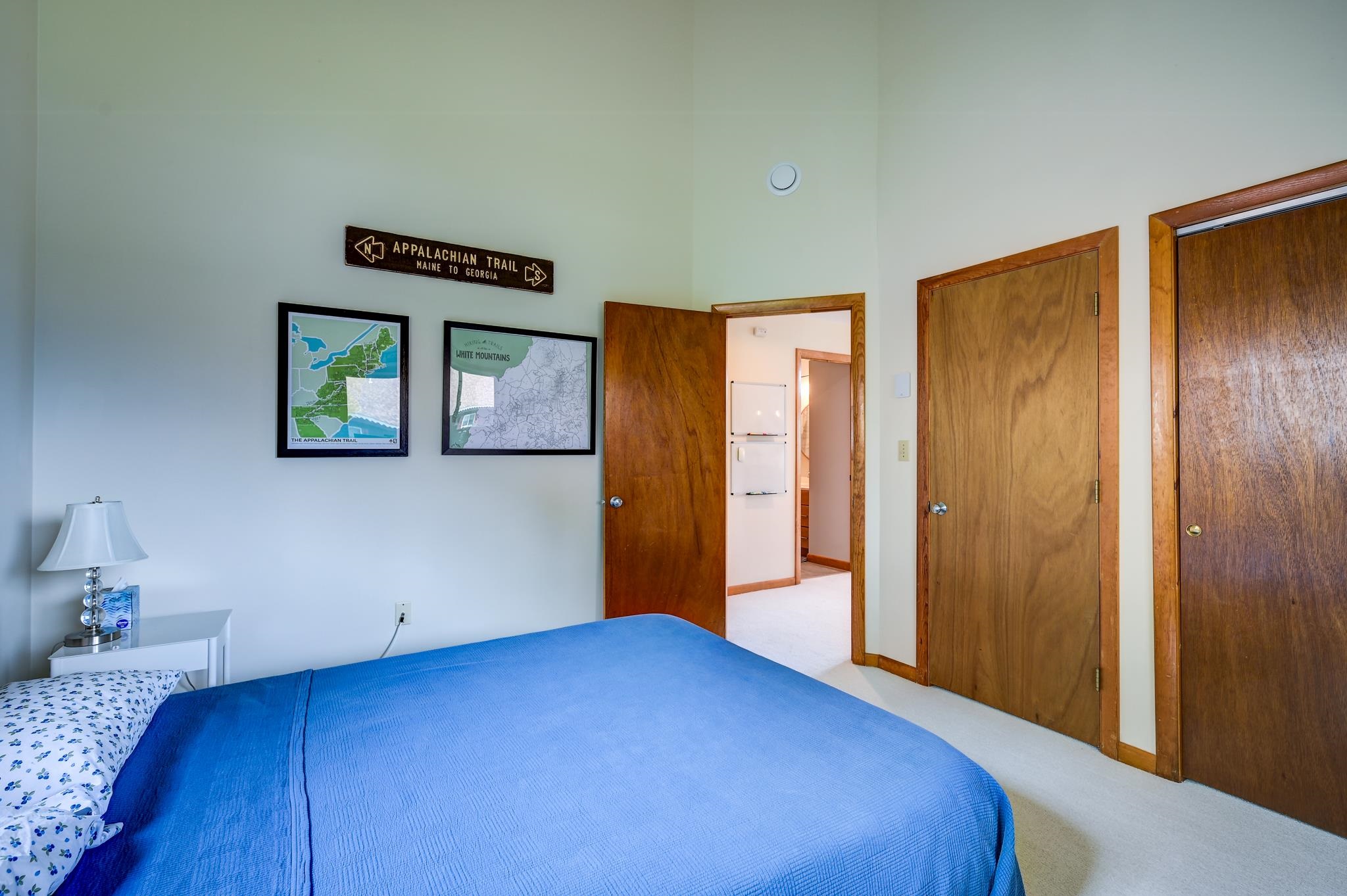 Bedroom with a blue bedspread, wooden doors, and Appalachian Trail maps on the wall.