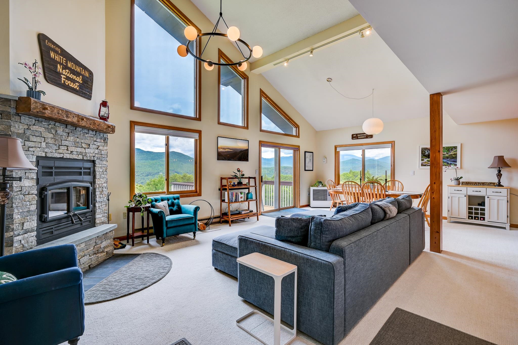 Vaulted living room with a stone fireplace, gray sectional, and mountain views through large windows.