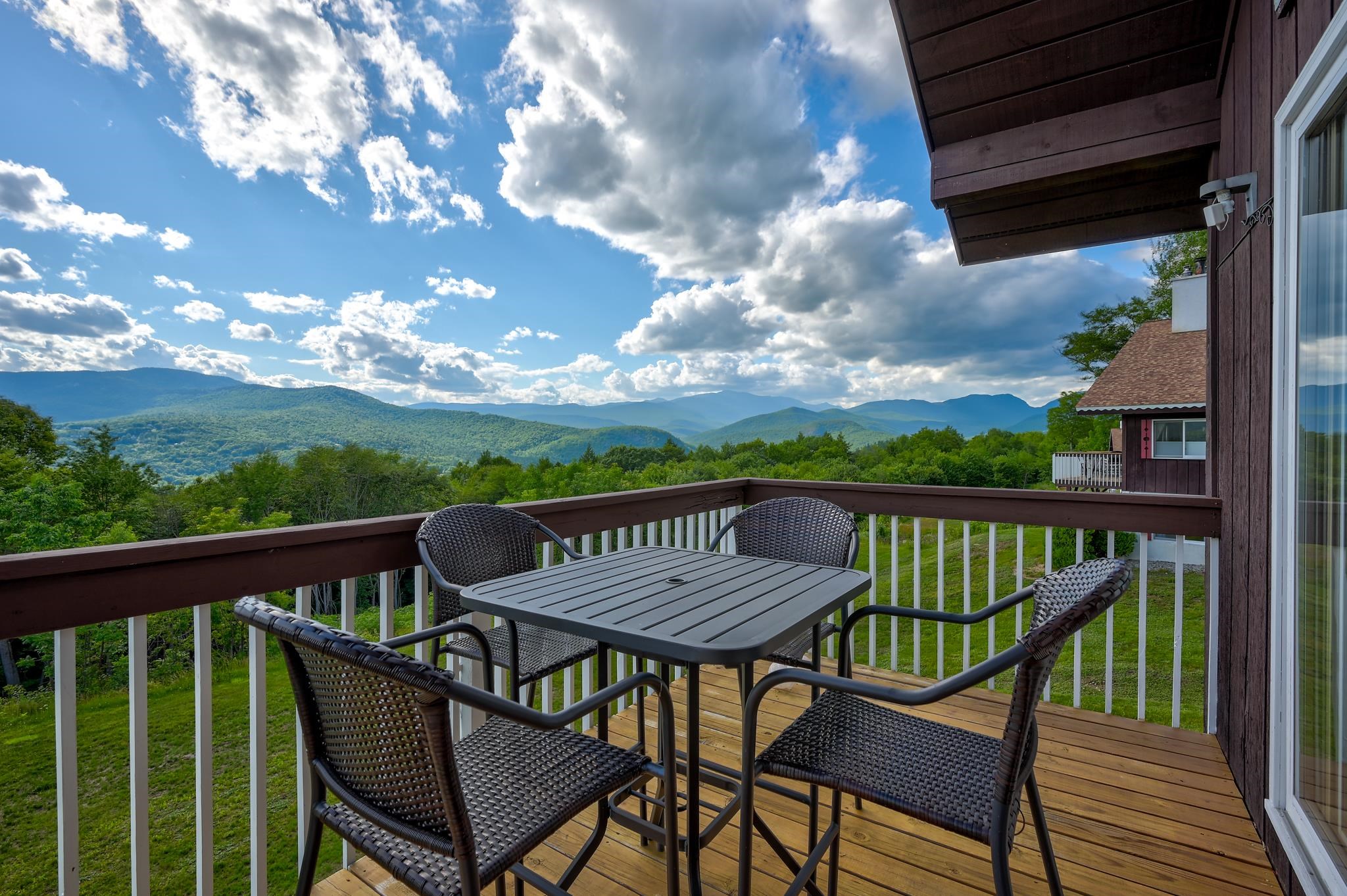 Deck with a table and four chairs overlooking forested mountain ridges.