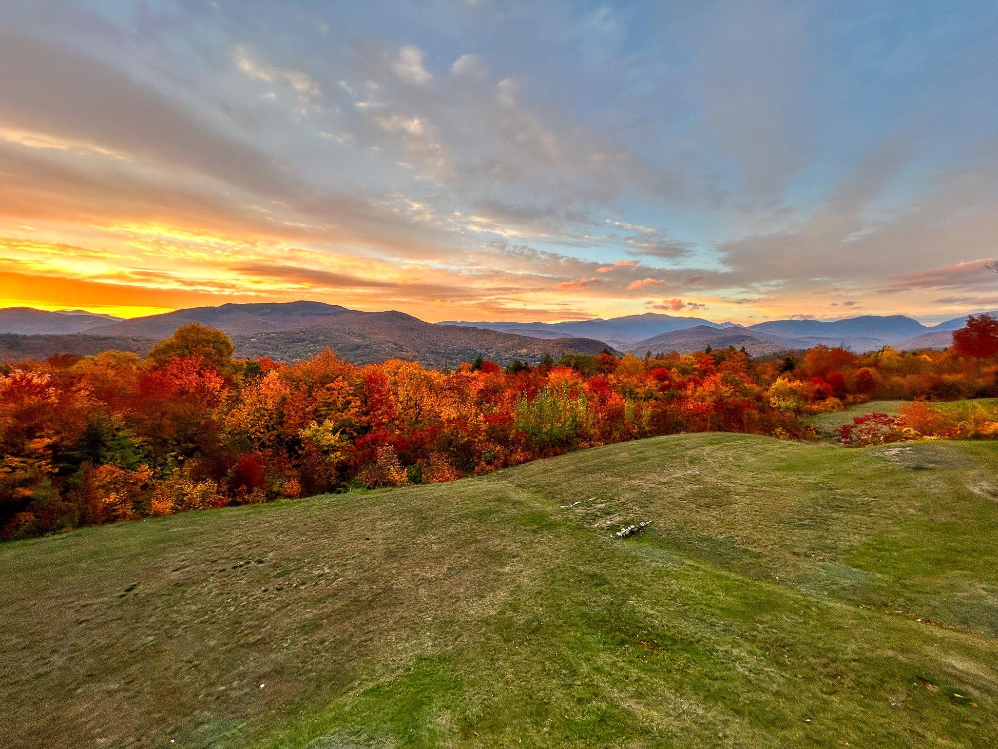 Mountain vista beyond a grassy lawn and brilliant autumn foliage at sunset.
