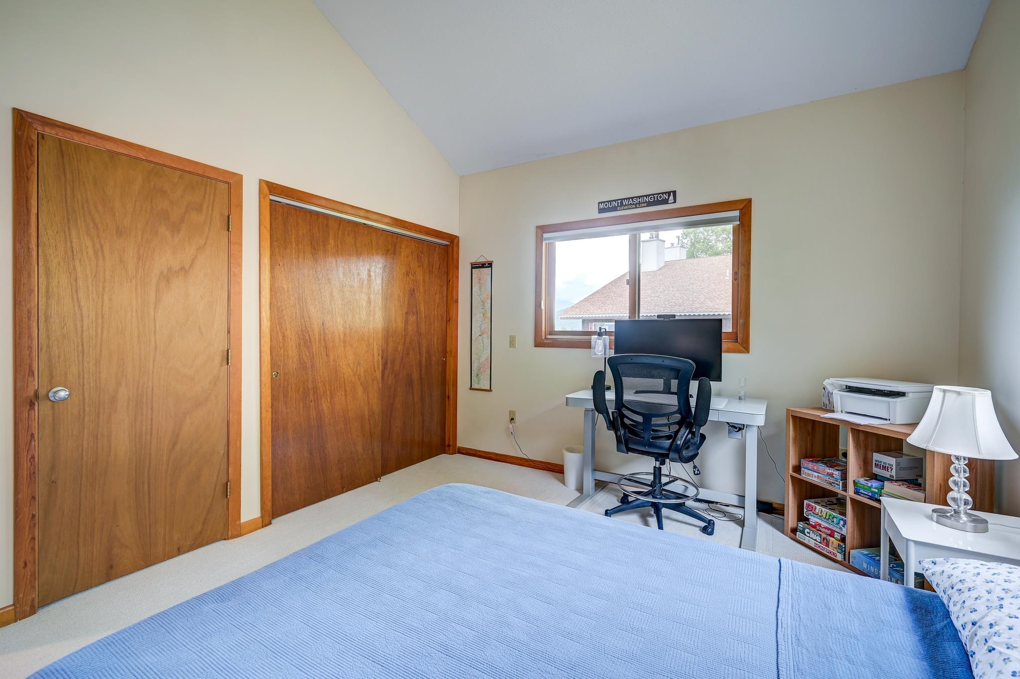 Bedroom with blue bedspread, wood closet doors, and a desk beneath a window.