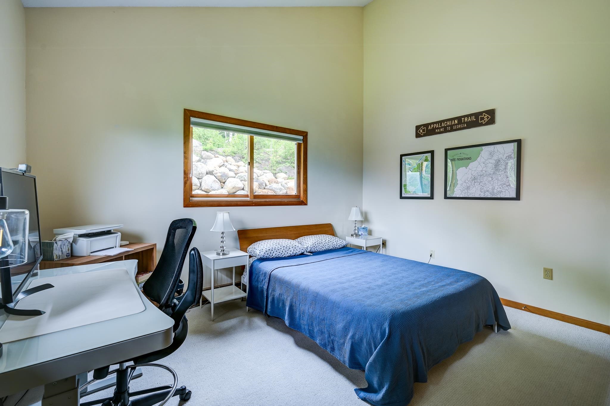 Bedroom with a blue-covered bed, office desk, and Appalachian Trail maps above the bed.