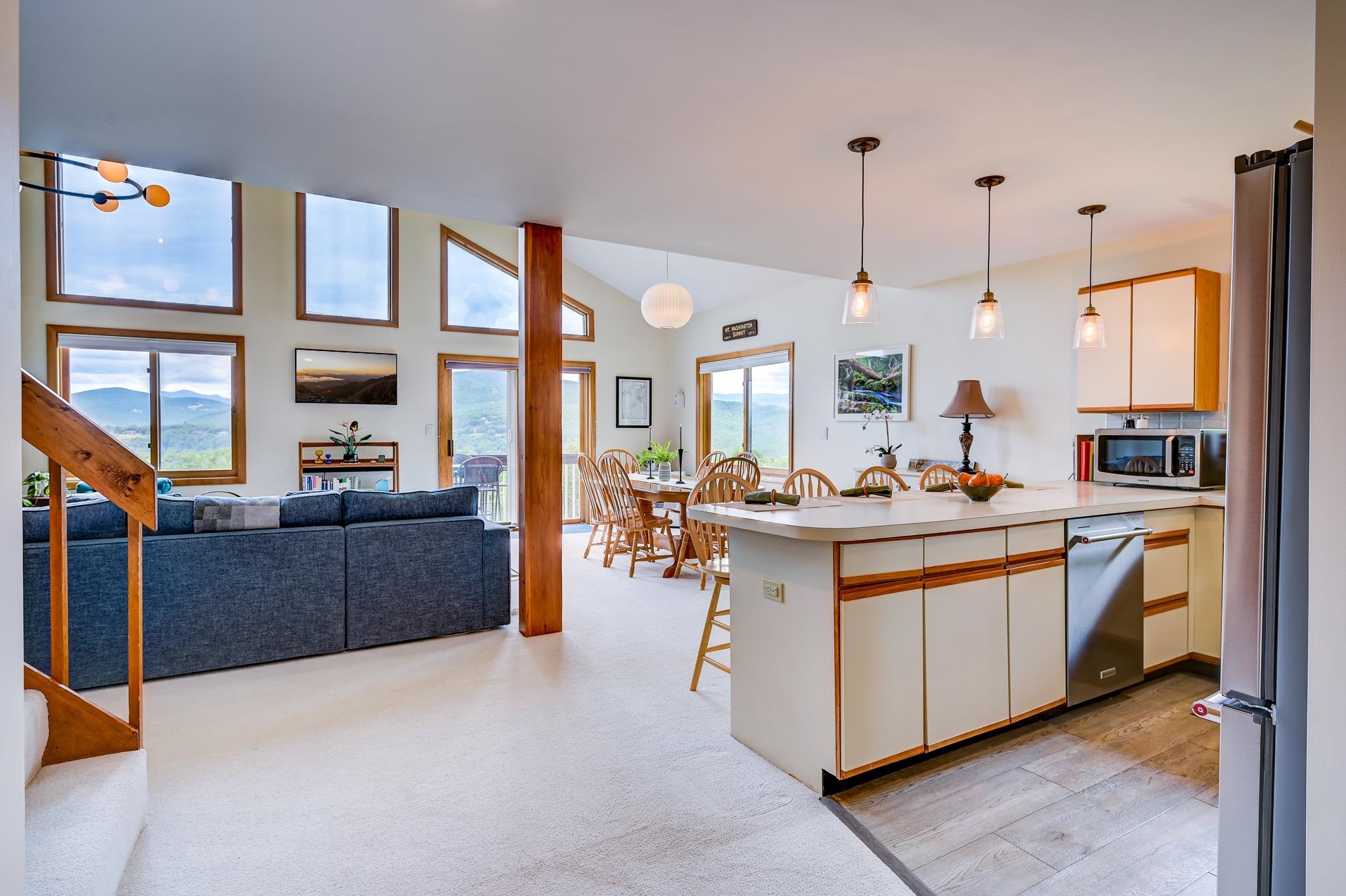 Open-plan living room and kitchen with a blue sectional and mountain views through large windows.