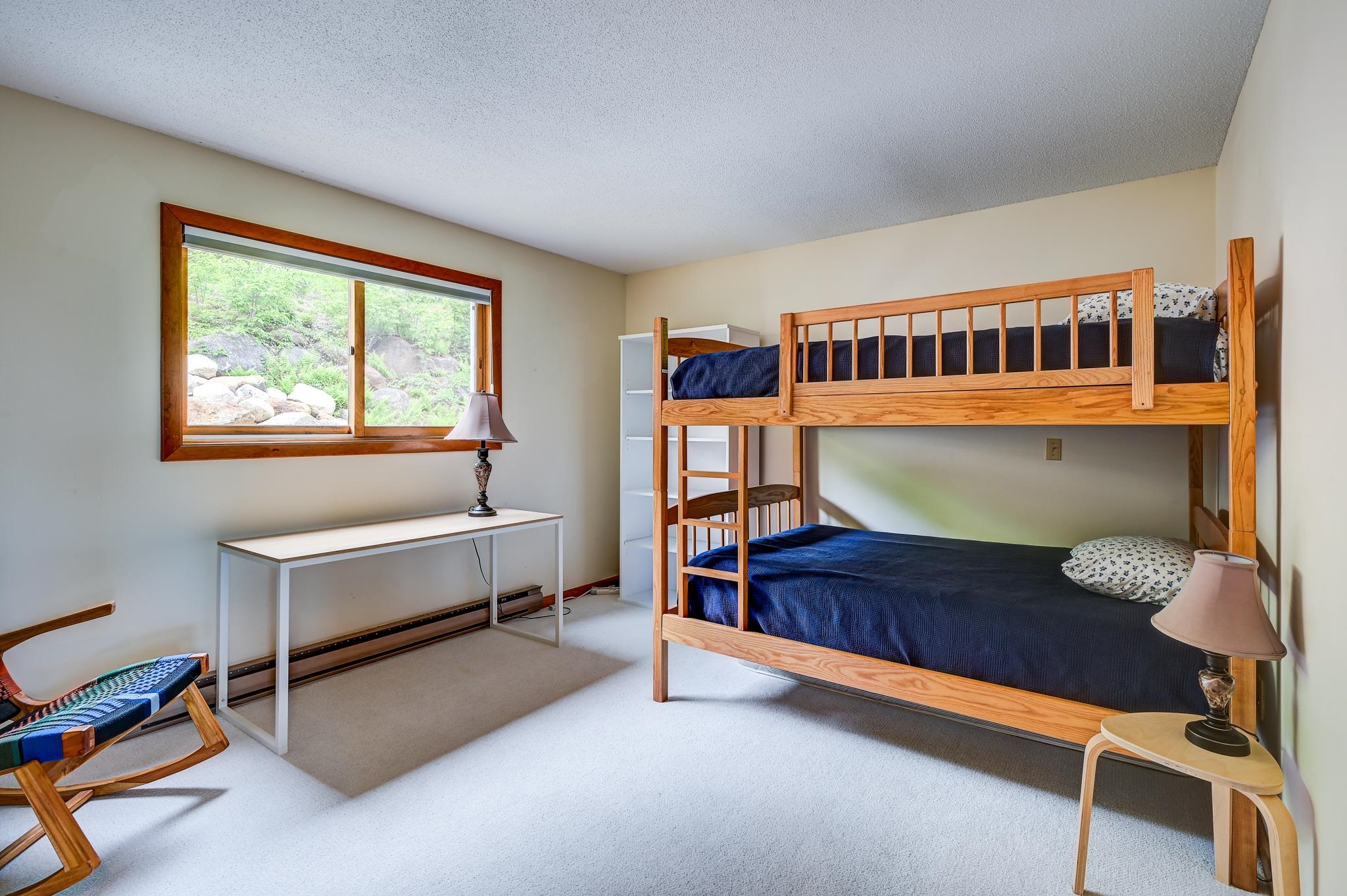 Bedroom with a wooden bunk bed, navy bedding, and a window overlooking greenery and rocks.
