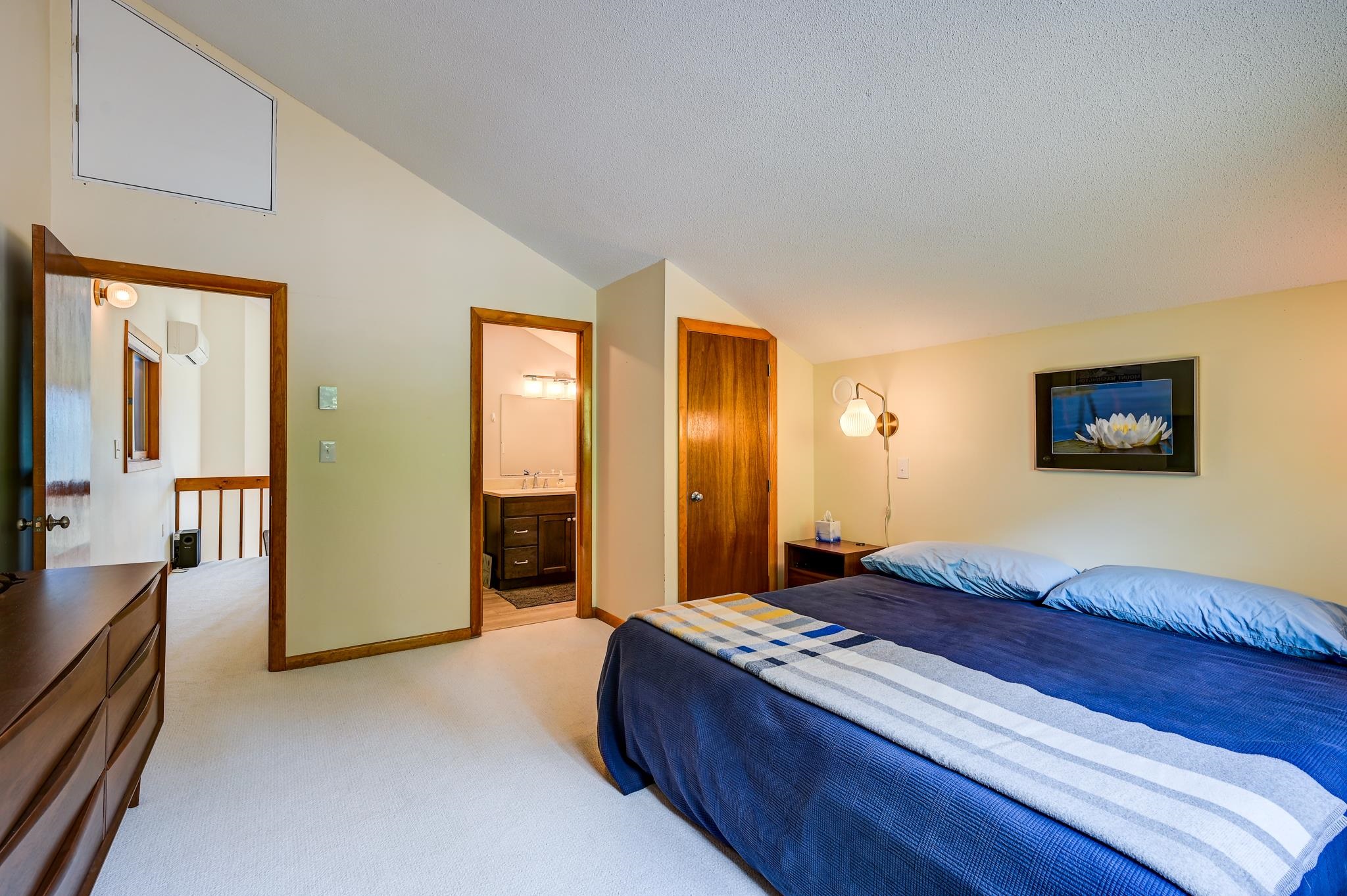 Bedroom with a blue-covered bed, sloped ceiling, and adjoining bathroom doorway.
