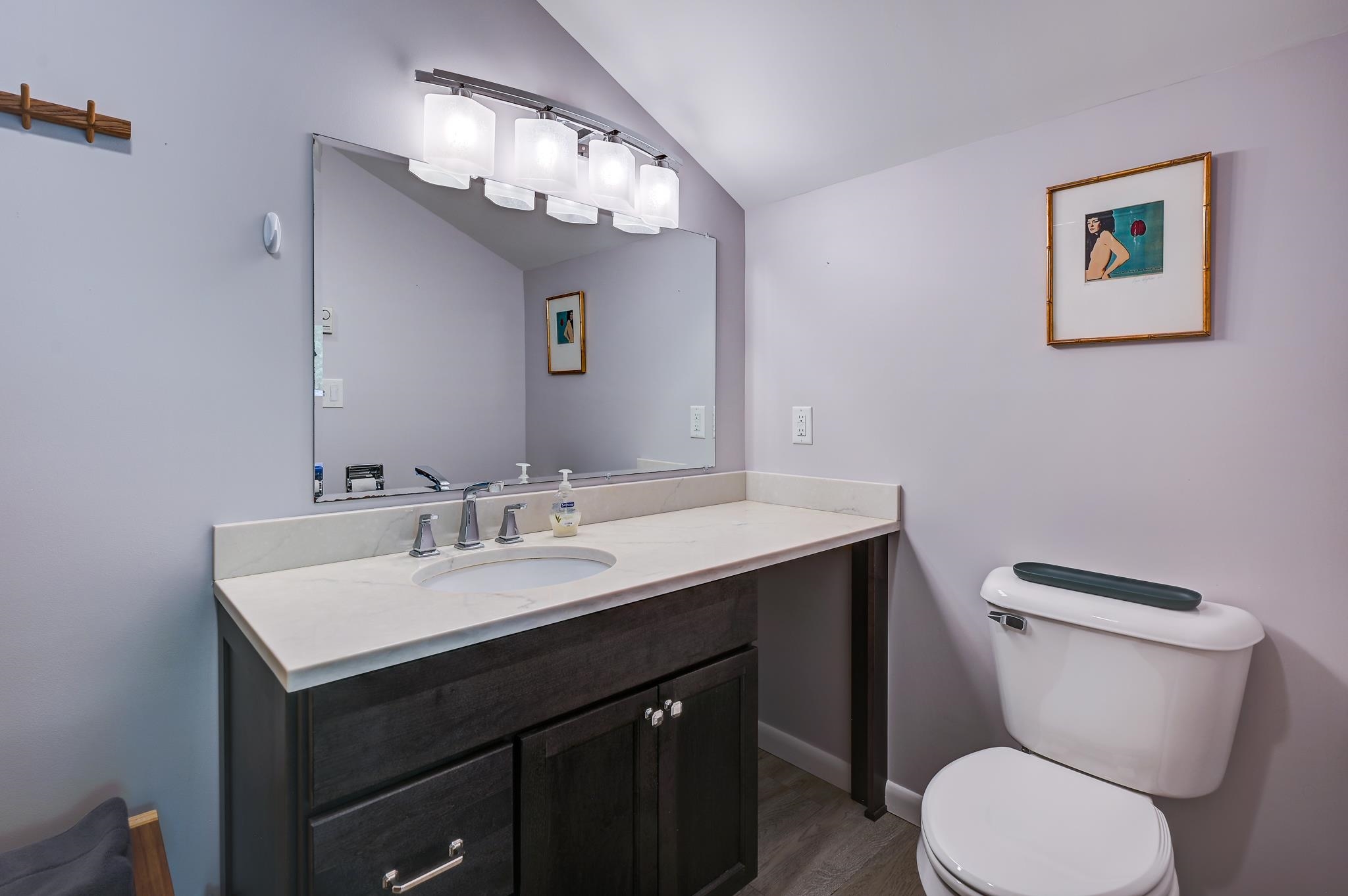 Bathroom with a dark wood vanity, white countertop, large mirror, and toilet.