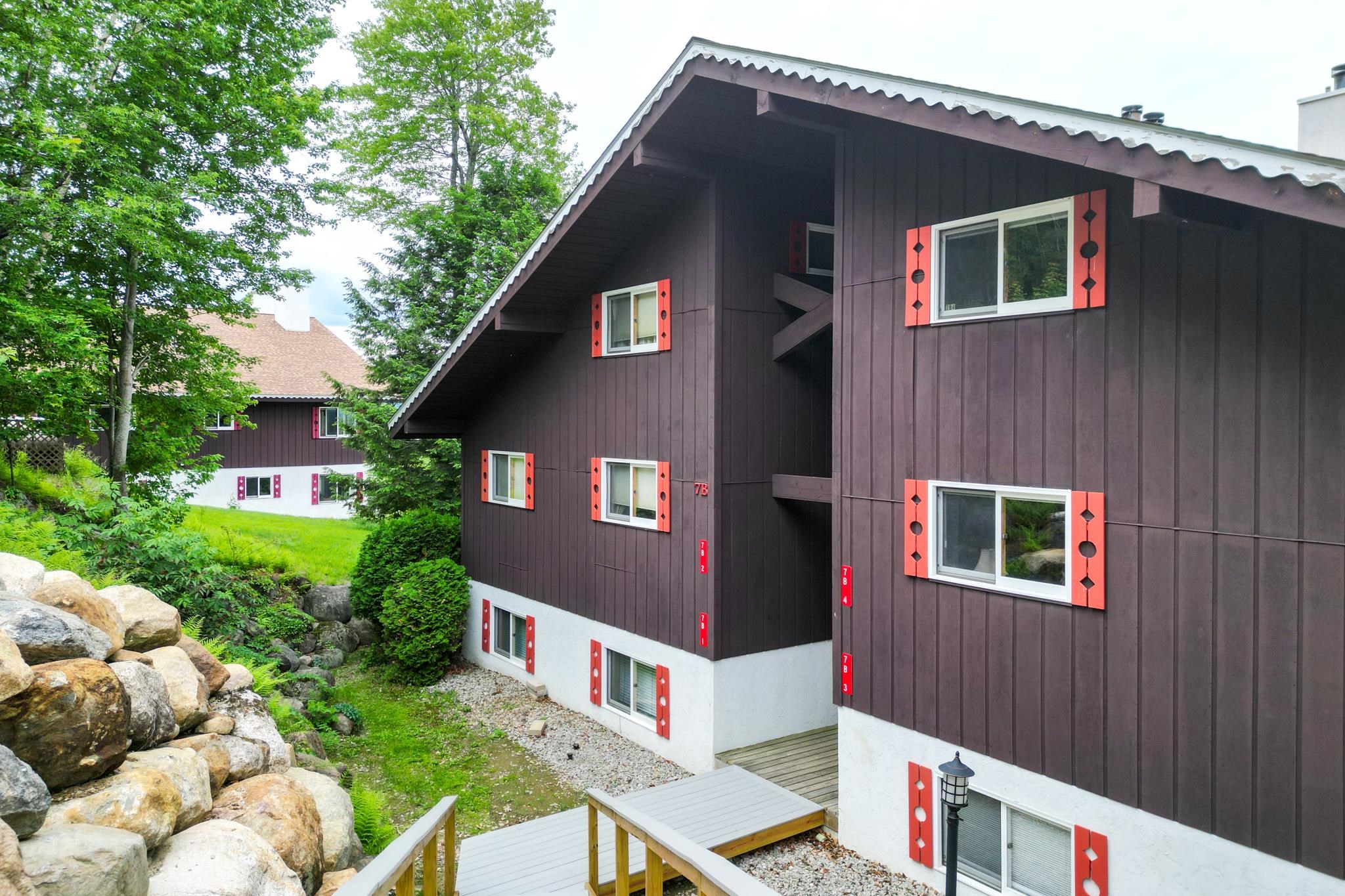 Condominium exterior with coral-red shutters, a wooden entry deck, and a landscaped rock garden.