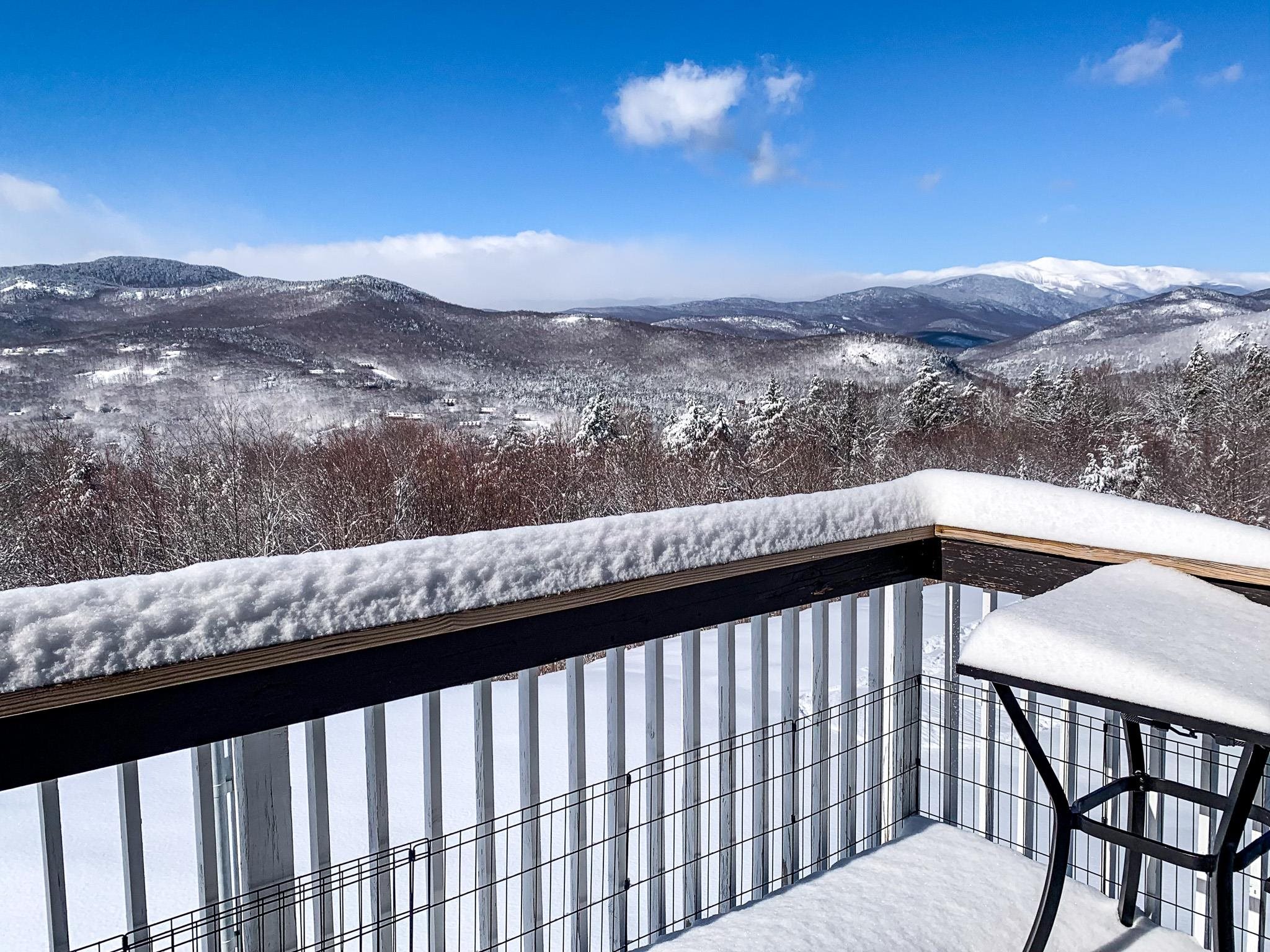 Snow-covered deck overlooking a mountain valley and distant lake.