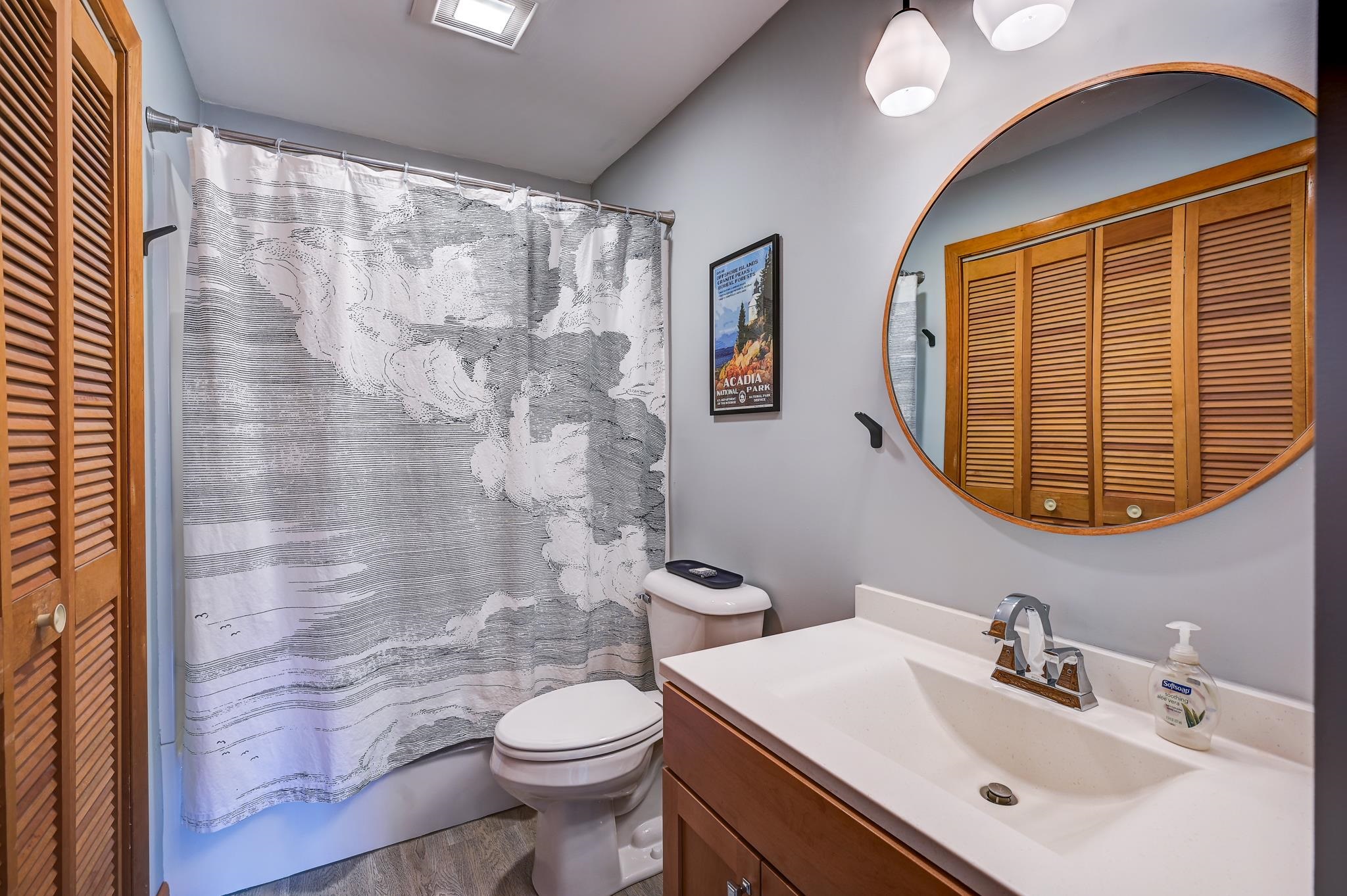 Bathroom with wood vanity, round mirror, and black-and-white patterned shower curtain.