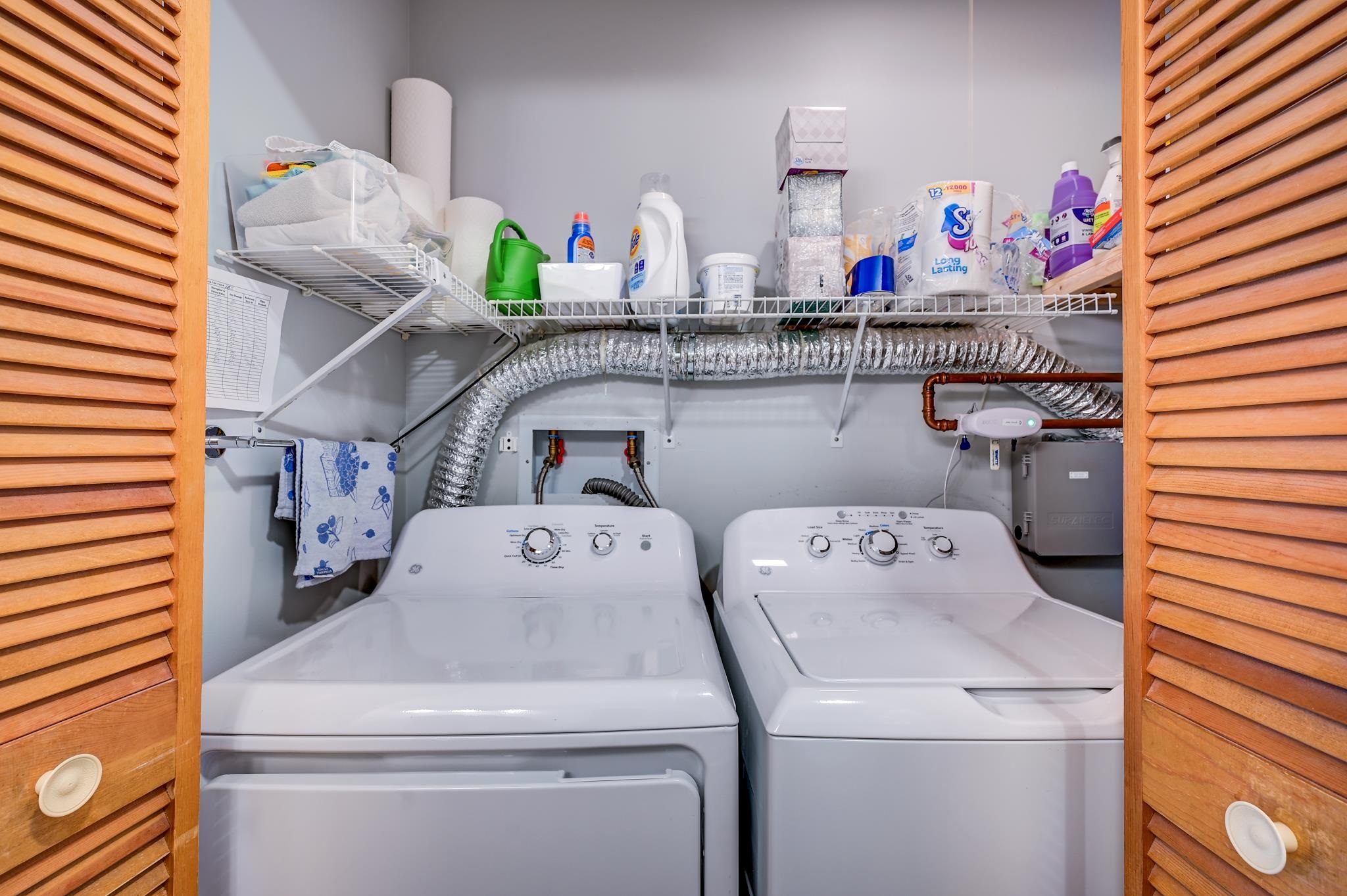 Laundry room with a white washer and dryer, wire shelves, and exposed ductwork.