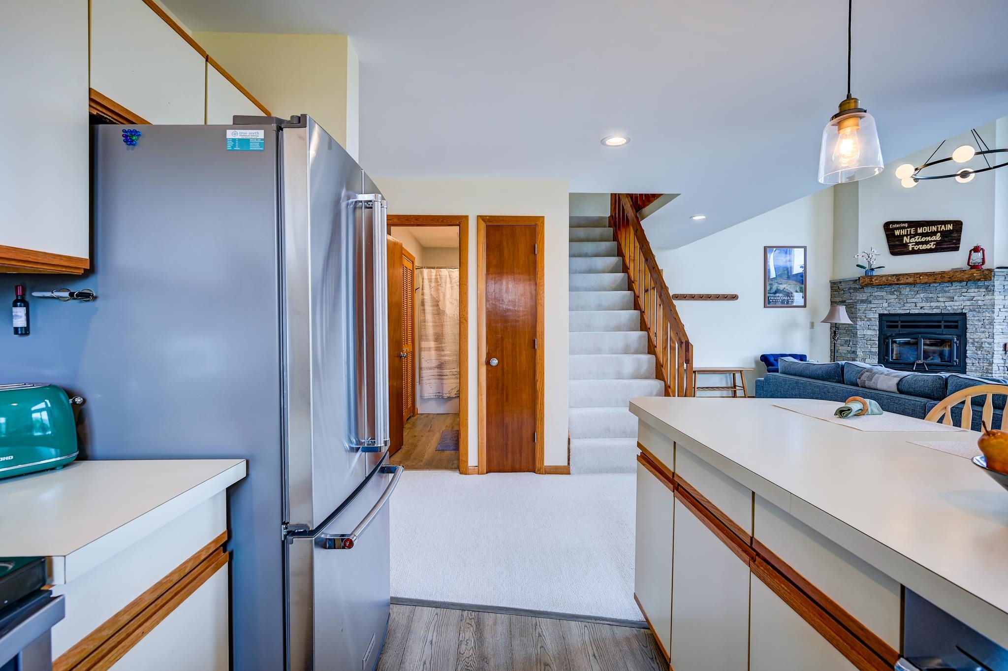 Open-plan kitchen and living room with a stone fireplace, blue sofa, and carpeted staircase.