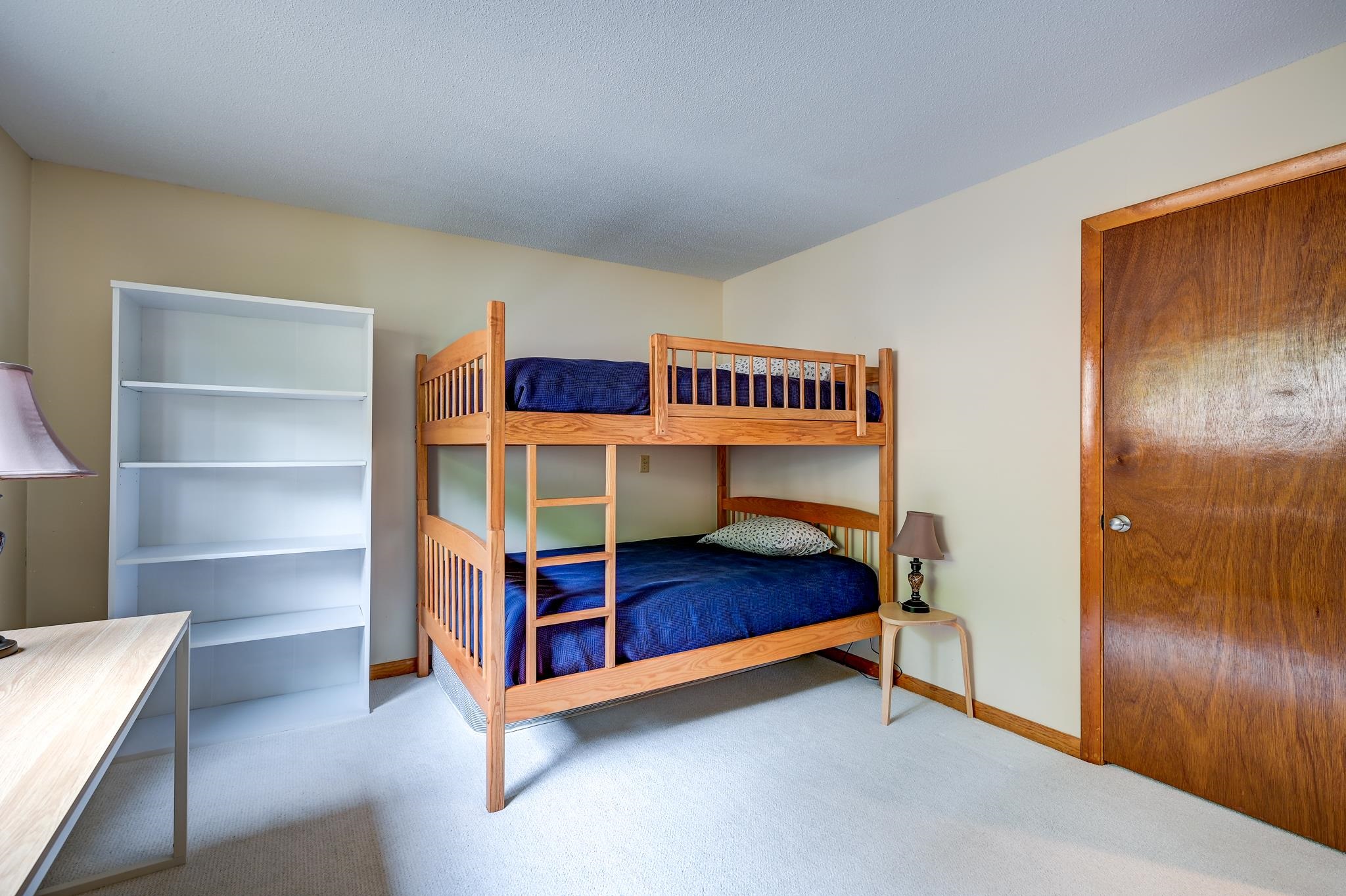 Bedroom with a wooden bunk bed, navy bedding, and an empty white bookcase.