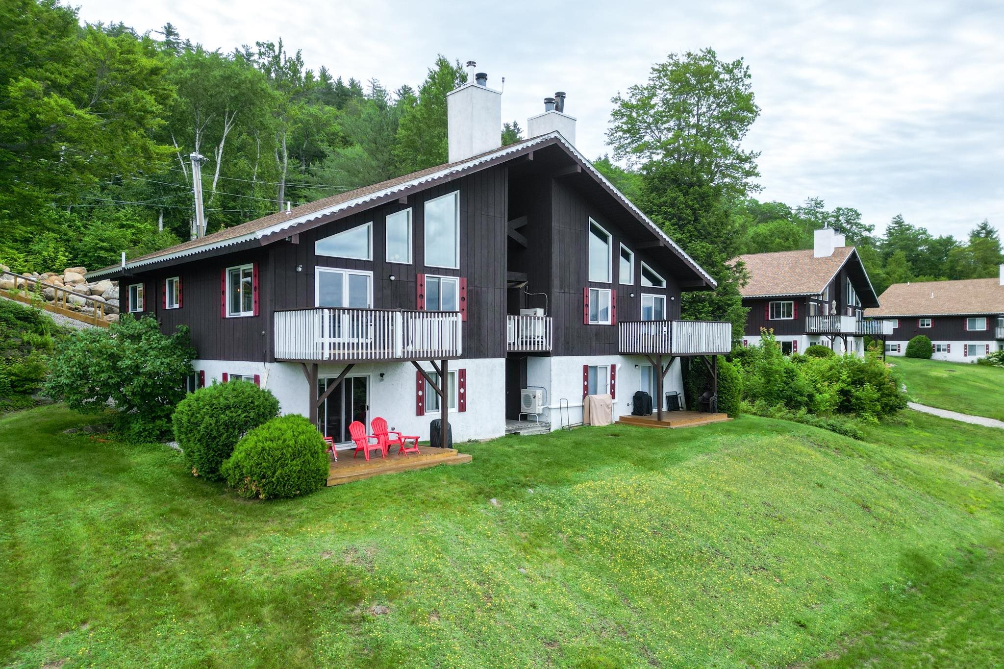 Dark-sided chalet-style home with white balconies, red shutters, and a lawn.
