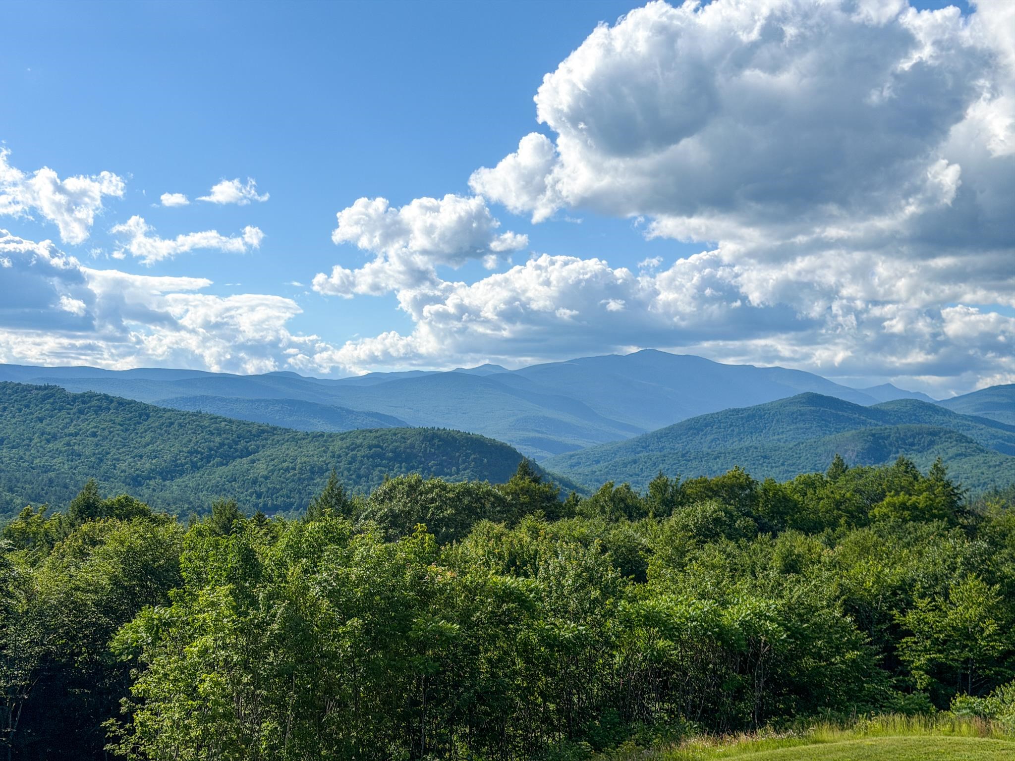 Panoramic view of forested mountain ridges beneath a blue, cloud-filled sky.