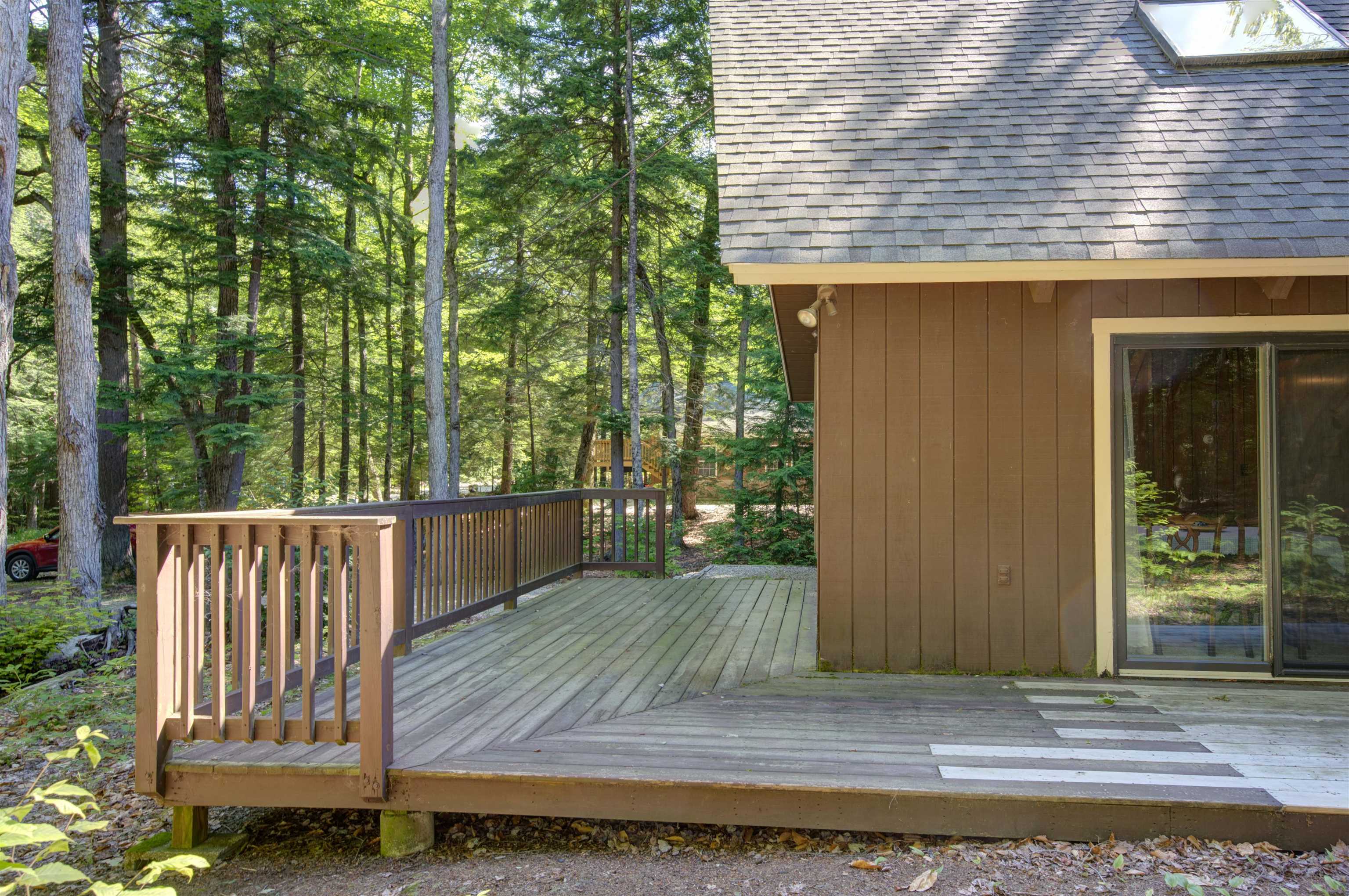 Wooden deck beside a brown-sided home, surrounded by trees and featuring a sliding glass door.