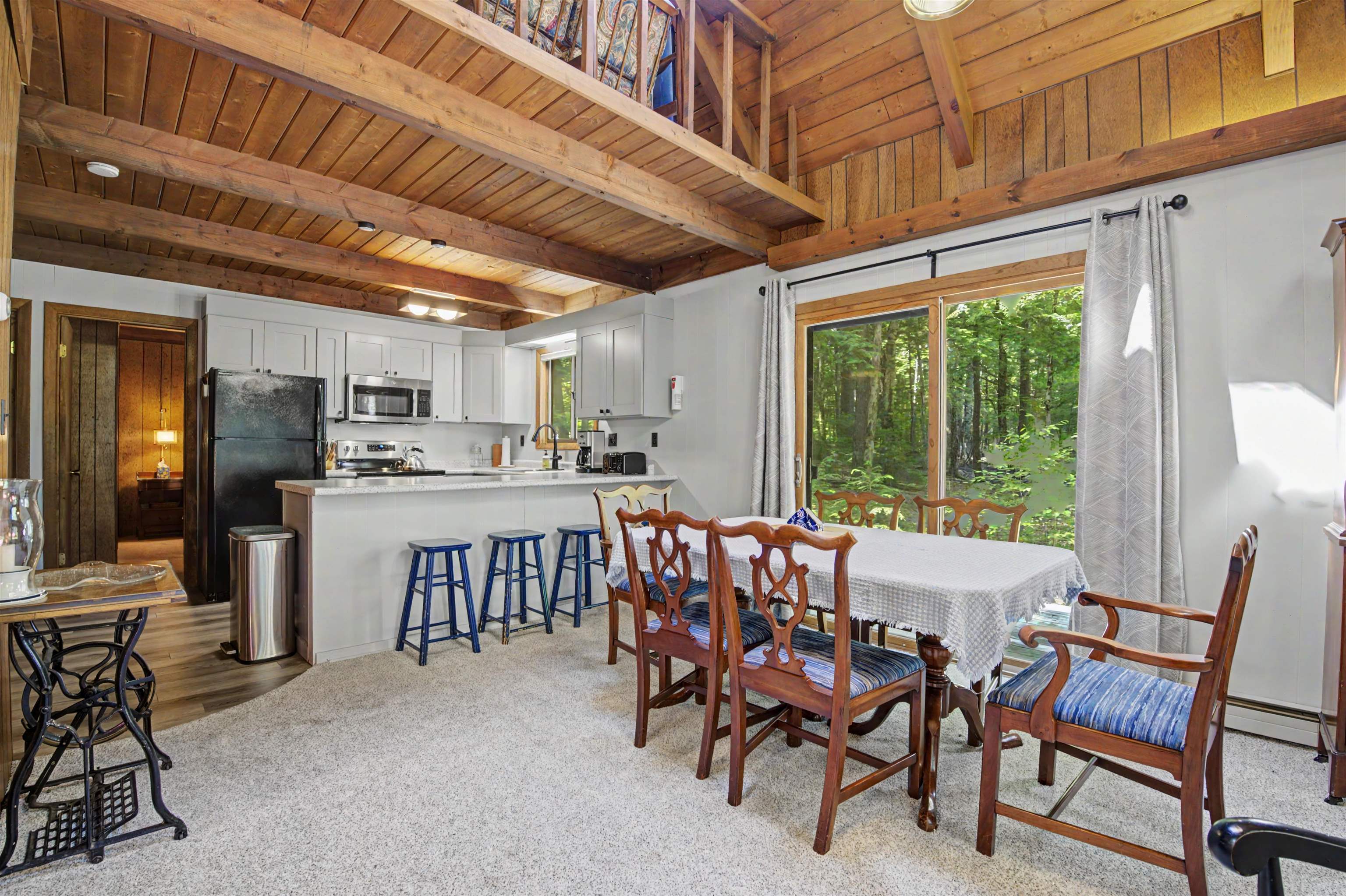 Open kitchen and dining area with exposed timber beams and sliding doors overlooking leafy woods.